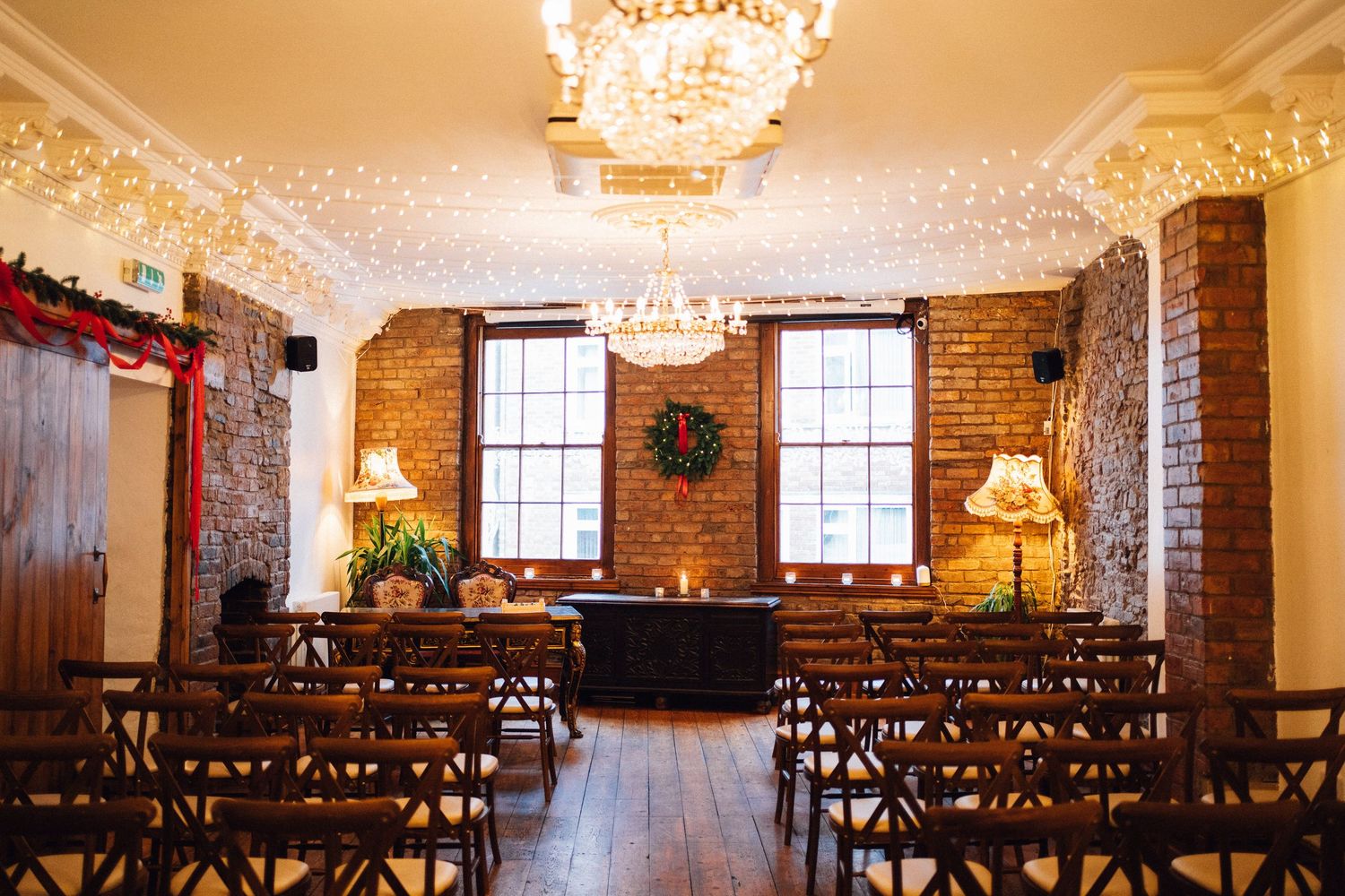 Elegant wedding ceremony venue with exposed brick walls, wooden chairs, and crystal chandeliers casting warm light.