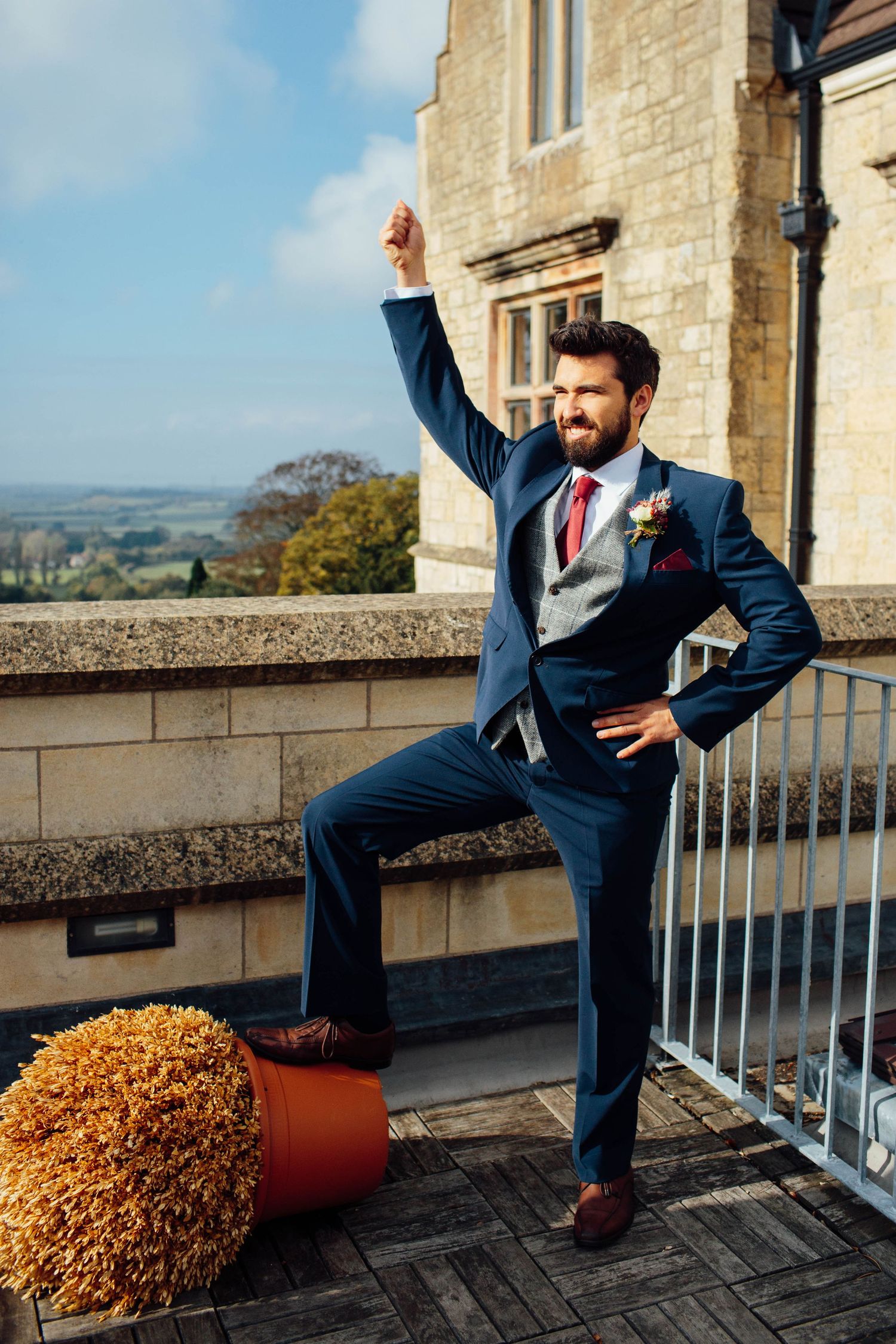 A person in a navy suit sits casually on a stone balcony with autumn foliage visible in a sequence of four poses.