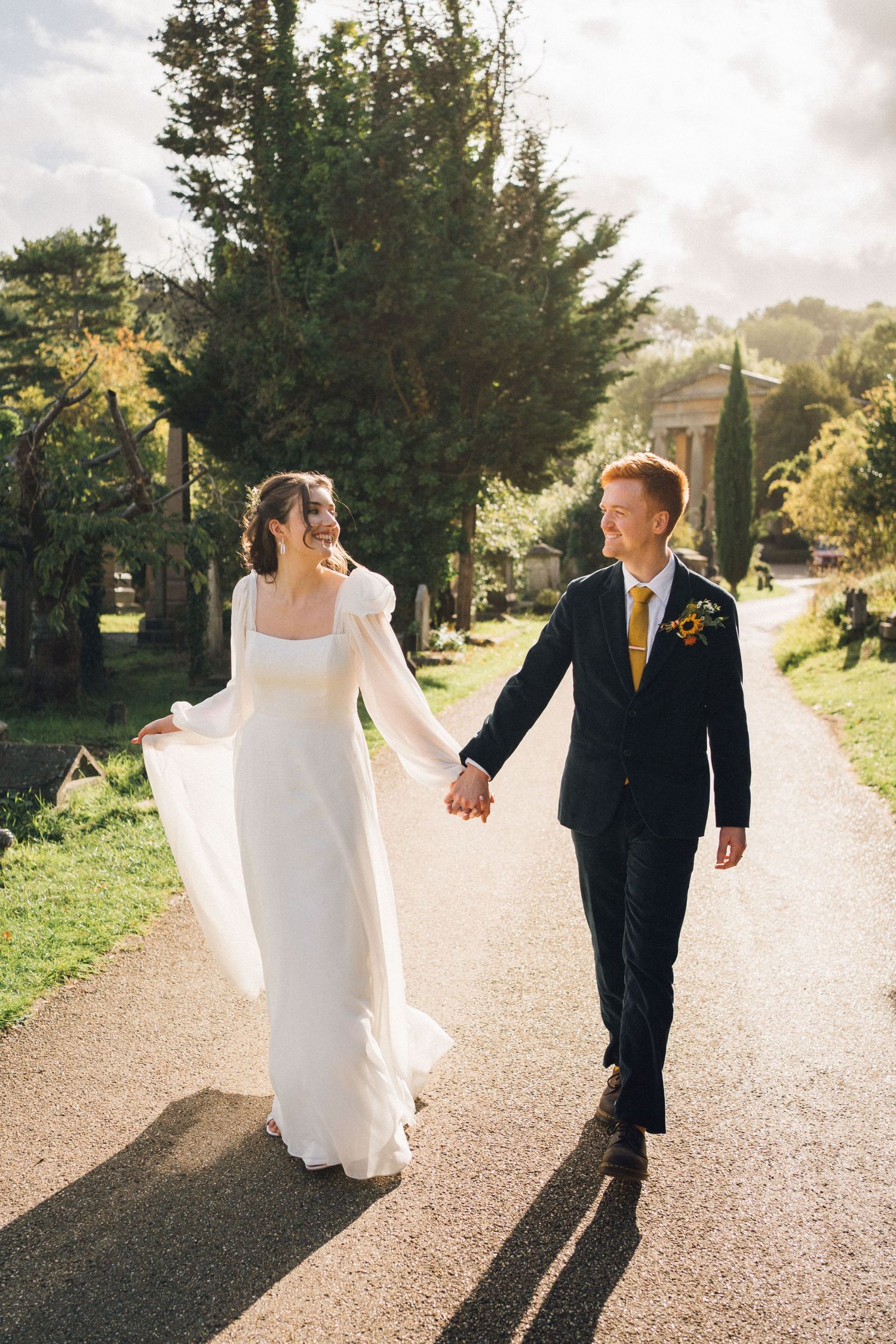 Couple walks hand in hand down a sunlit path on their wedding day.