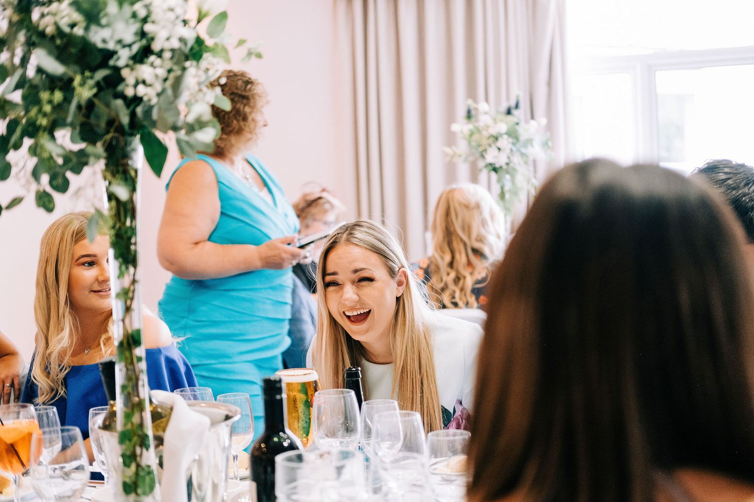 Wedding guests mingling and celebrating in a bright reception venue with floral decorations.