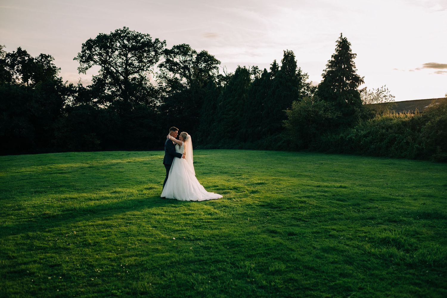 Scenic outdoor wedding photos taken in a lush green field at sunset.