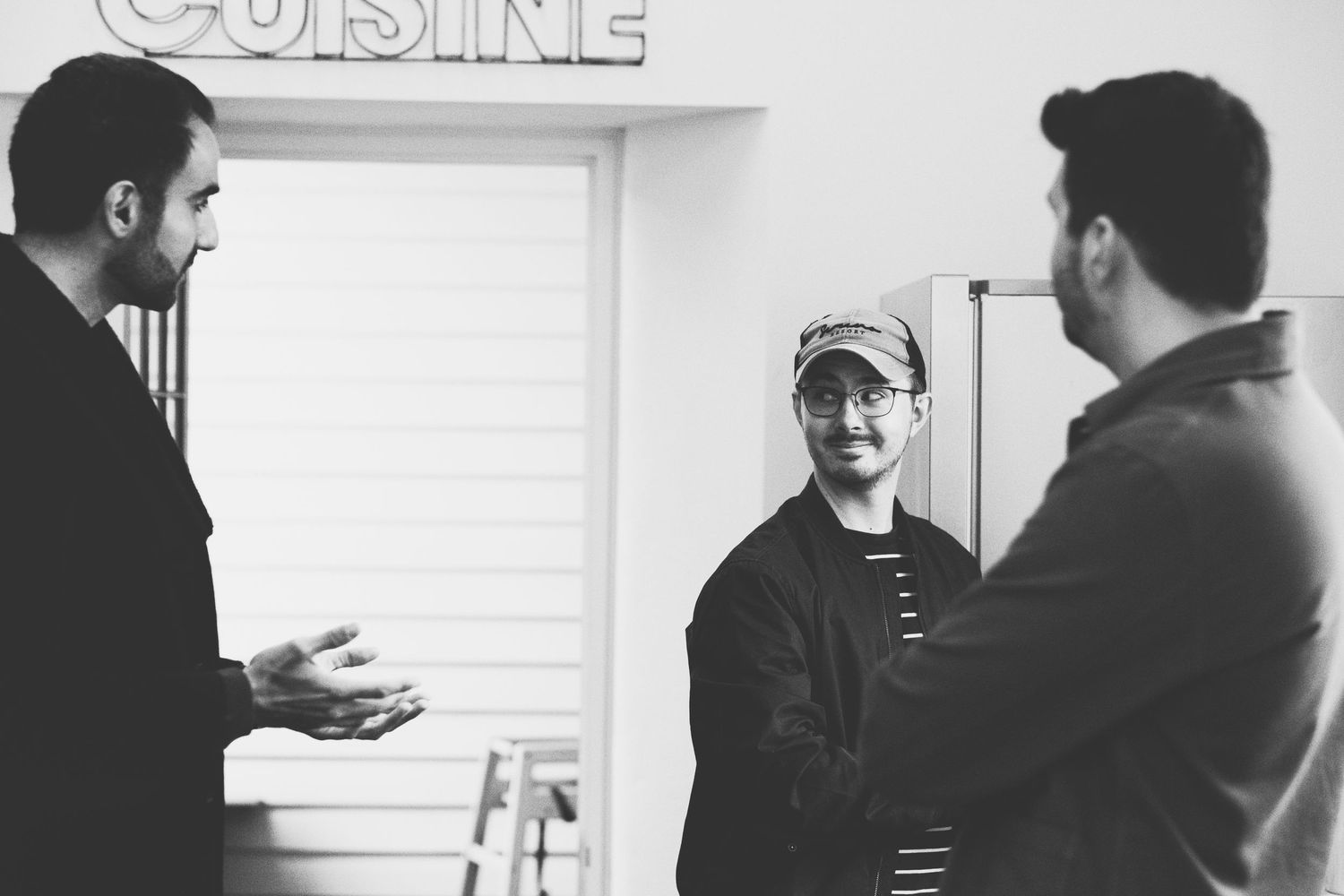 Three people having a conversation in a kitchen with 'Cuisine' text visible on the wall.