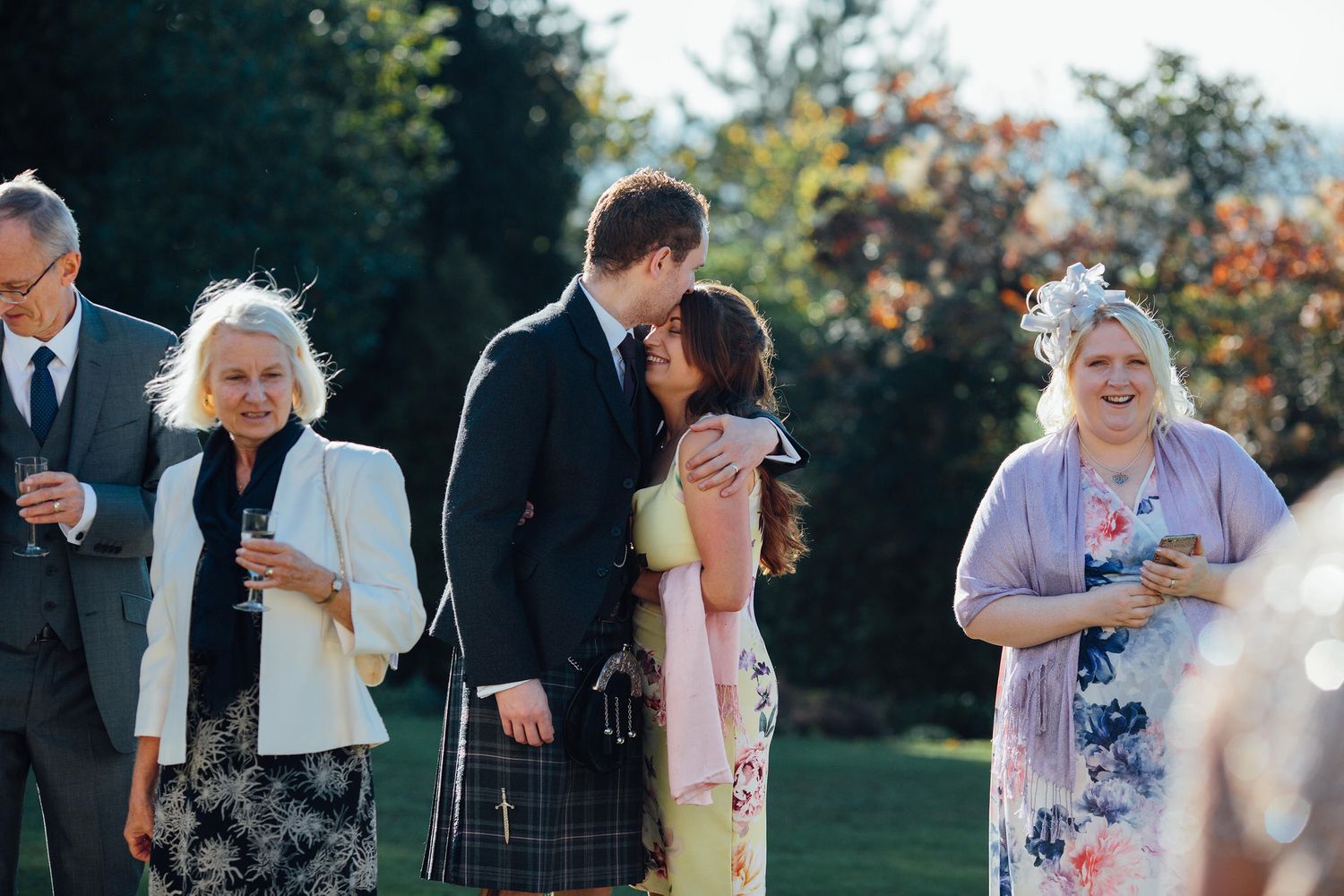 Wedding guests gather outdoors for casual conversation during a reception.