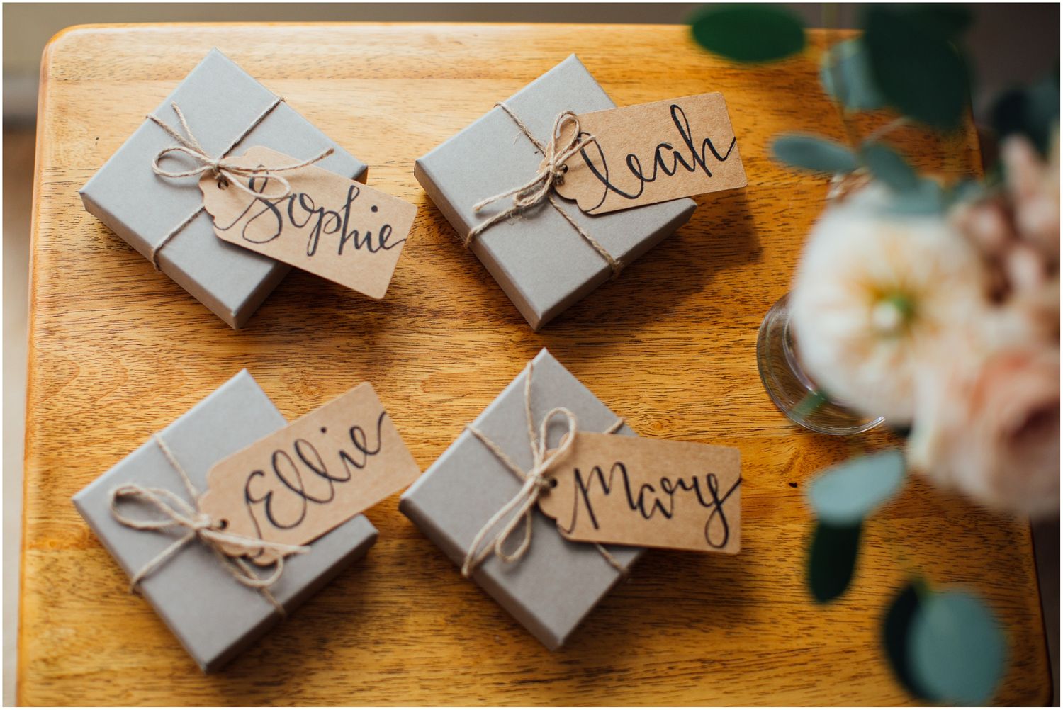 Small wrapped packages with handwritten name tags arranged on a wooden surface.