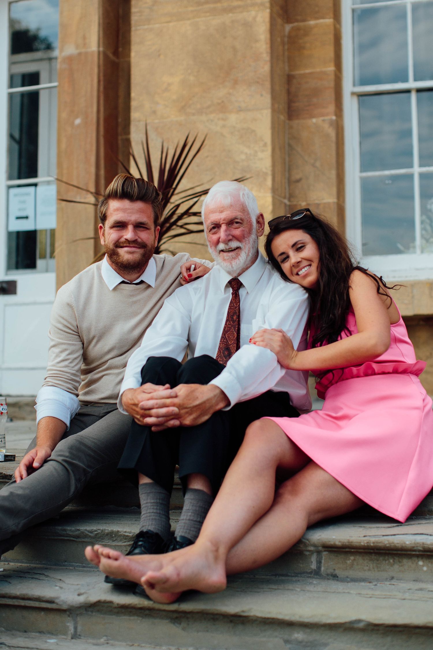 Three people sitting together on stone steps outside a building.