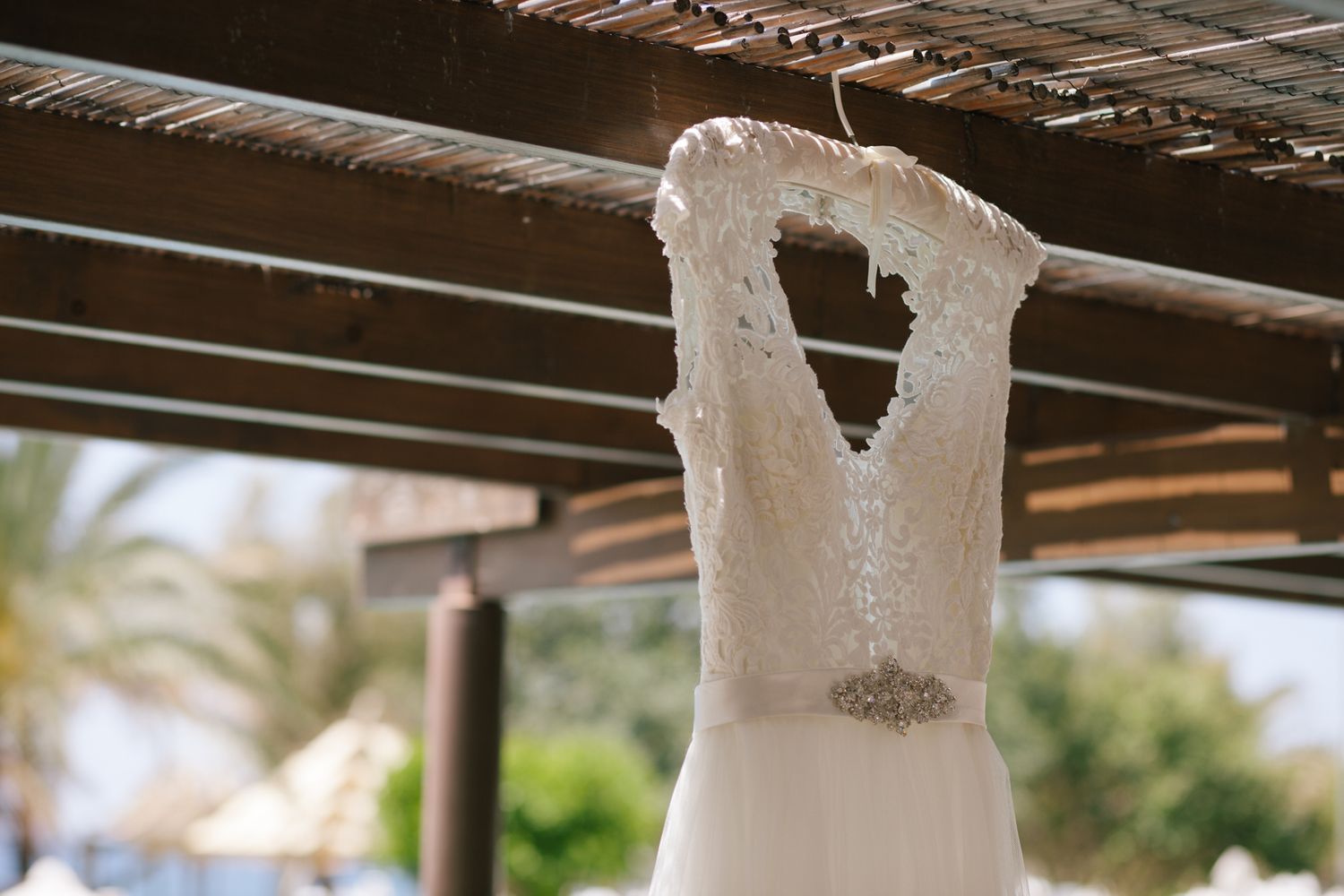 White lace wedding dress hanging from wooden beams with natural lighting.