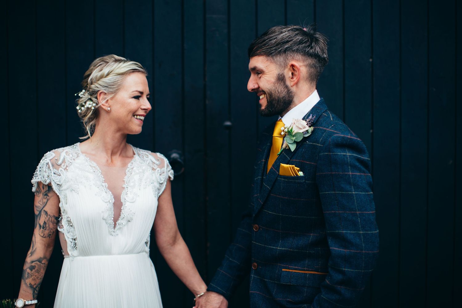 Wedding couple in navy suit and lace dress pose together against a dark backdrop.