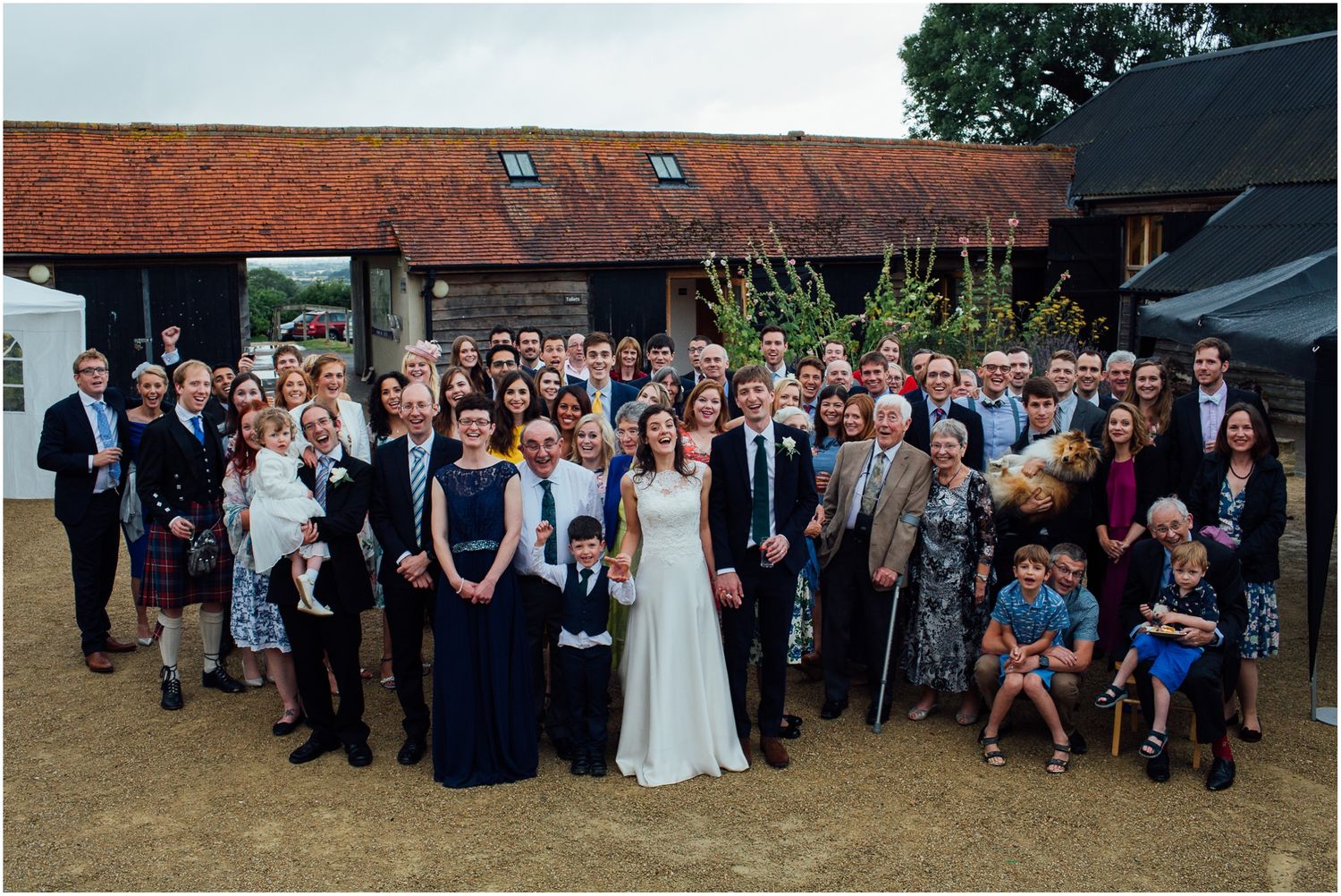 Large group photo of wedding guests gathered outside a rustic brick building.