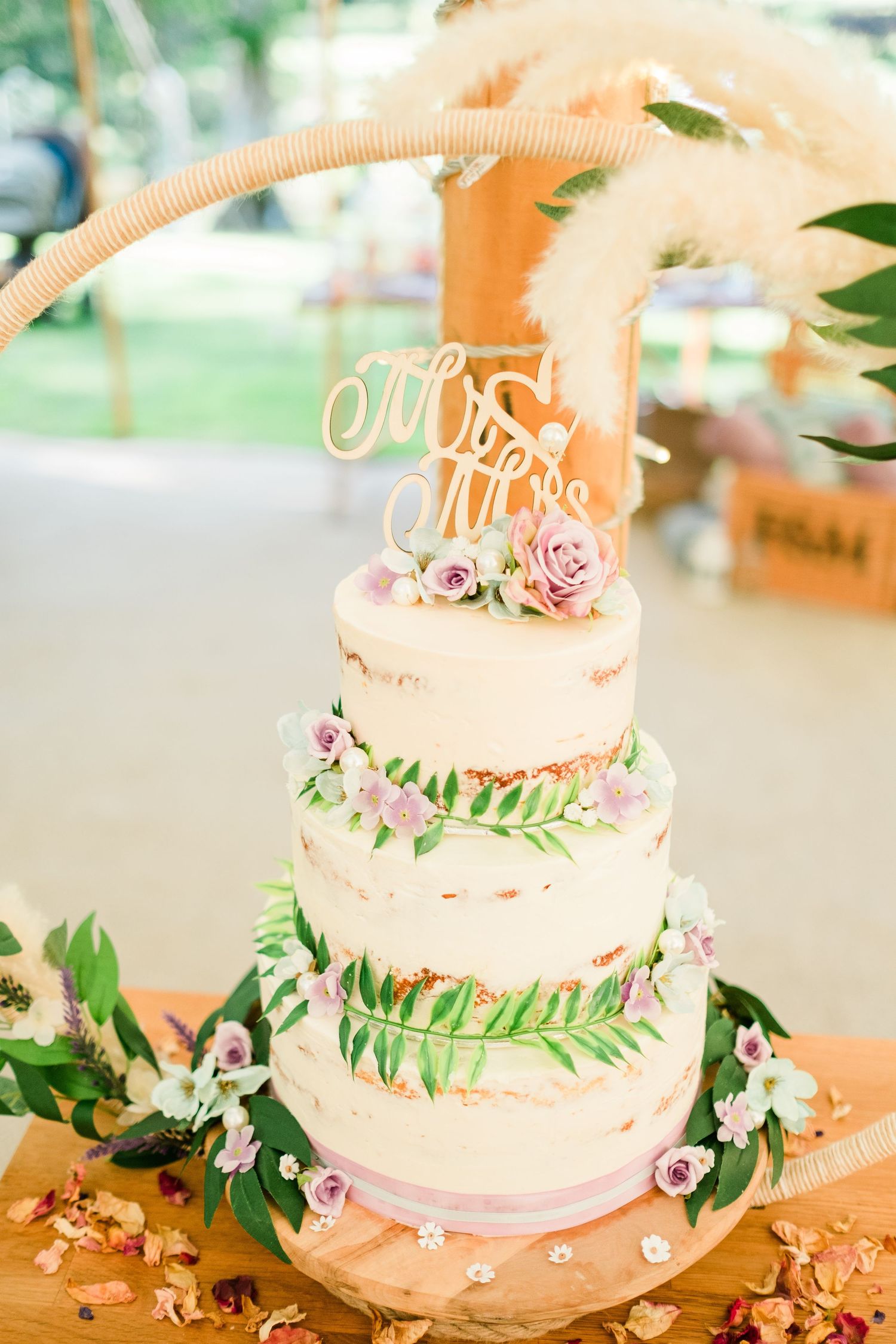 Elegant three-tier wedding cake decorated with pink roses and greenery on a white tablecloth.