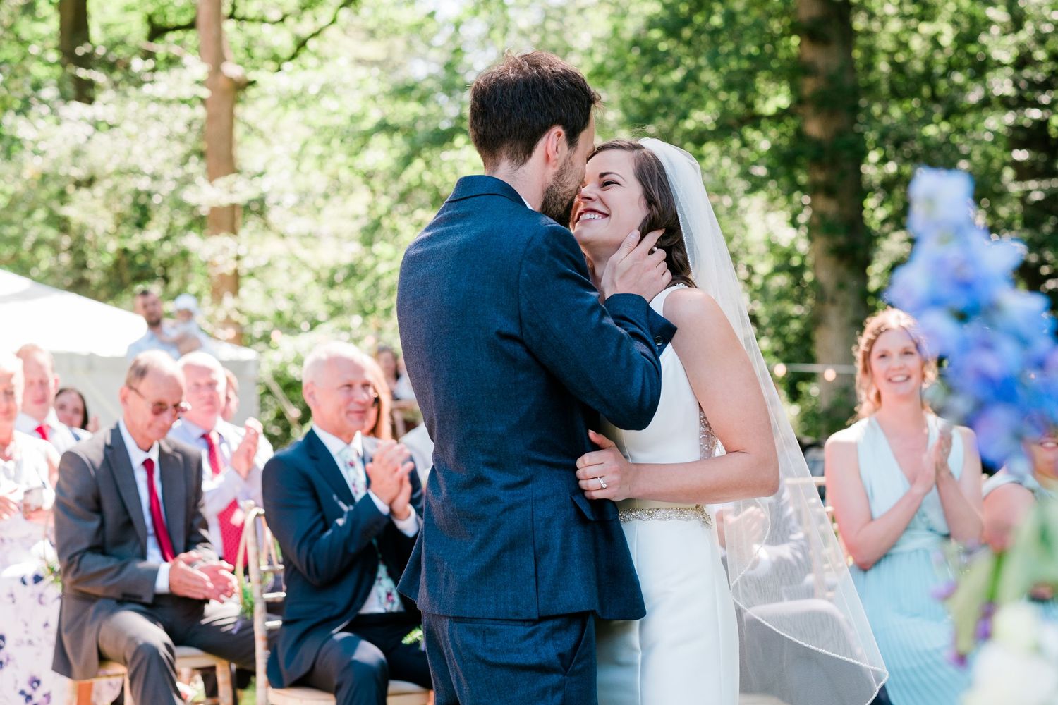 Wedding guests celebrate during an outdoor garden reception with blue balloons and natural greenery.