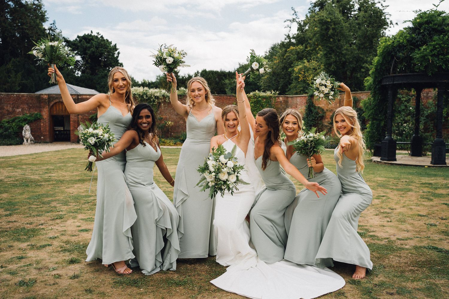 Bridesmaids in flowing gray gowns dancing and laughing during wedding photoshoot.
