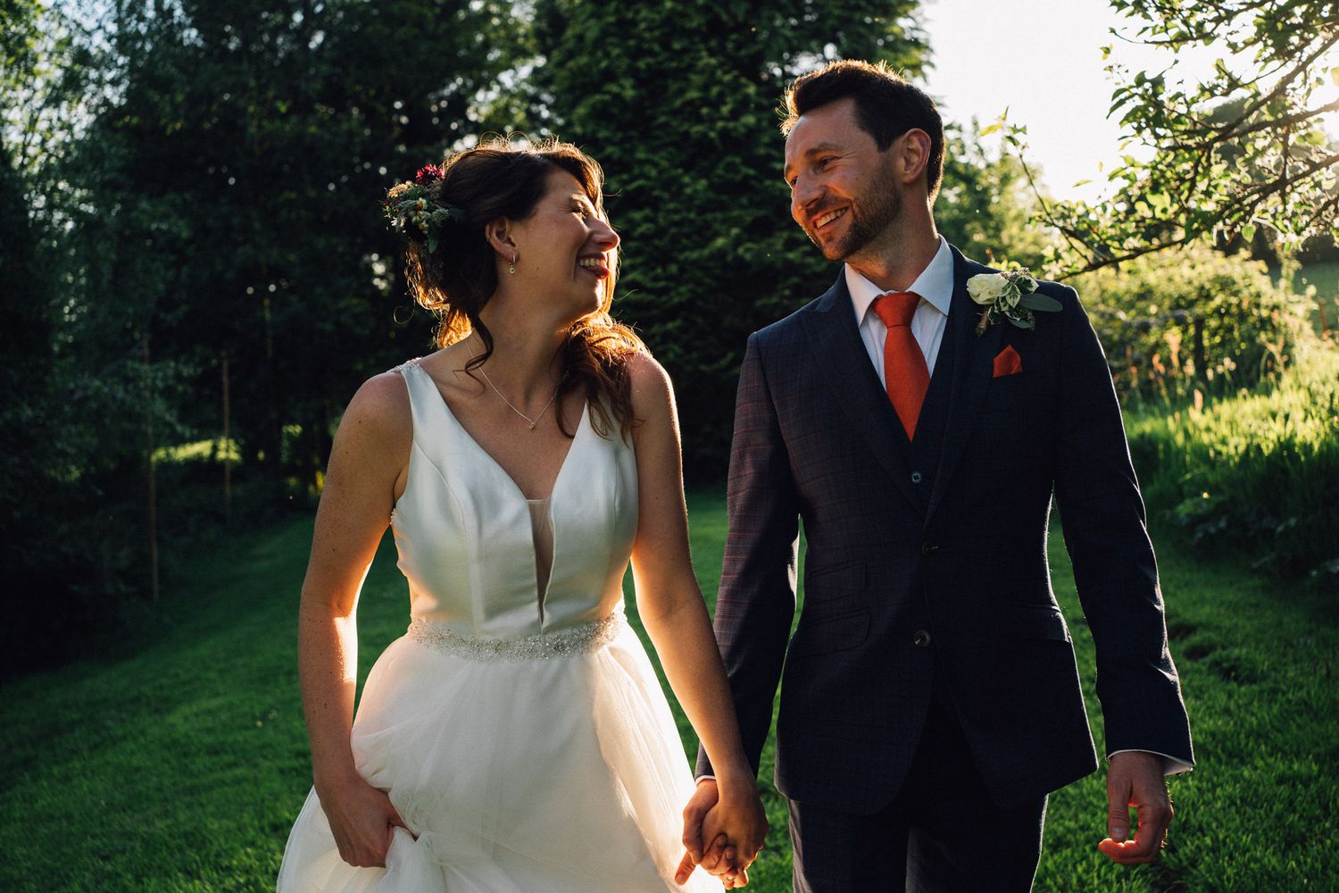 Couple walking together in a lush green outdoor setting during golden hour.