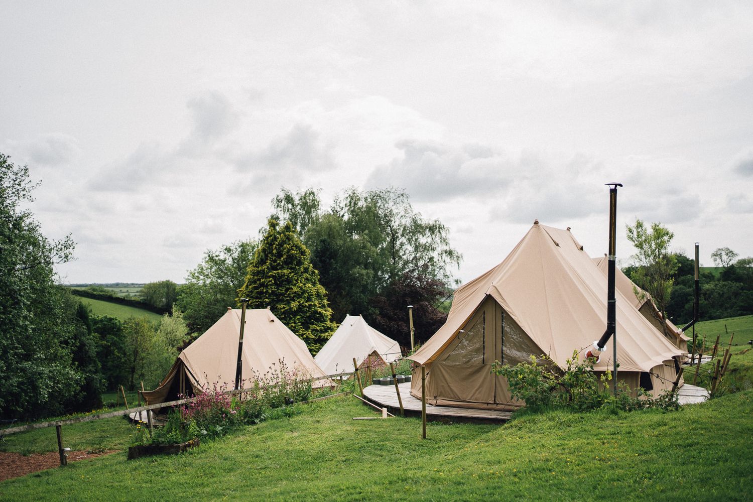 Row of bell tents set up in a green field for glamping at a wedding venue.