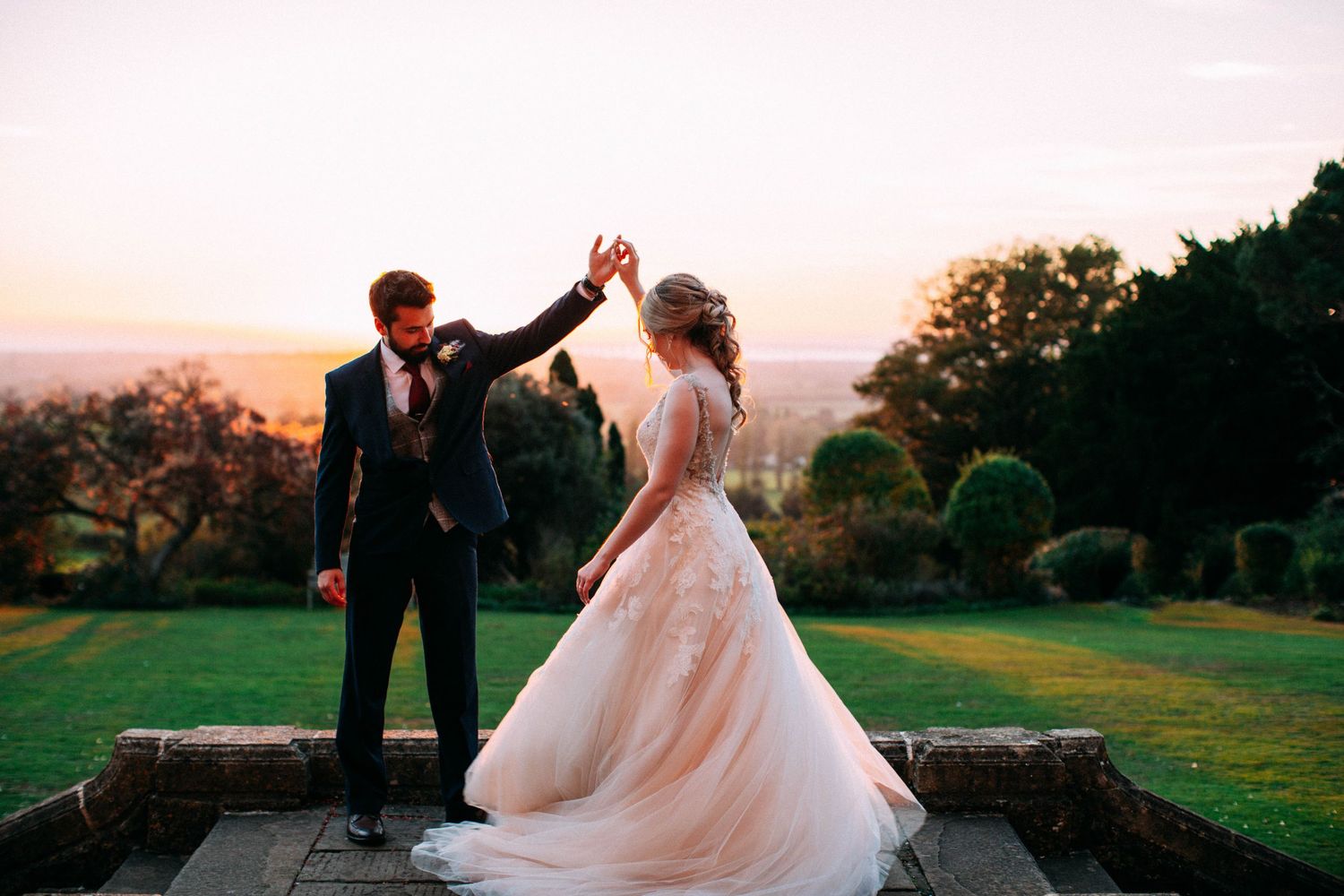 A couple in wedding attire embraces on a scenic golf course at sunset, with golden light illuminating the landscape.