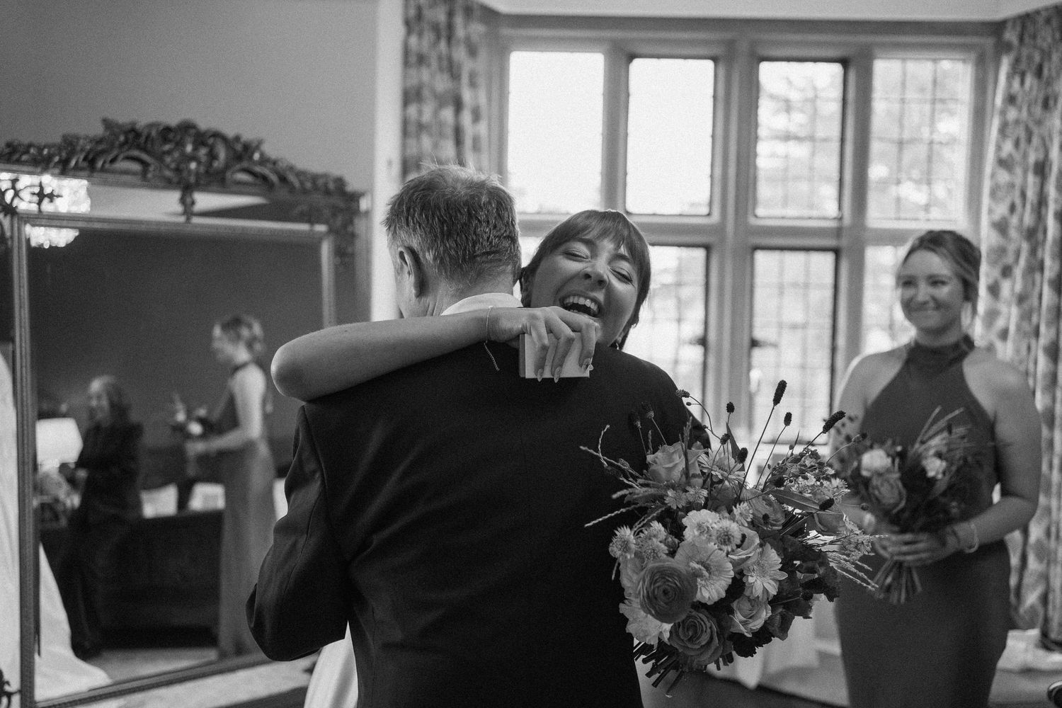 A black and white wedding photo showing an emotional embrace while holding floral bouquets.