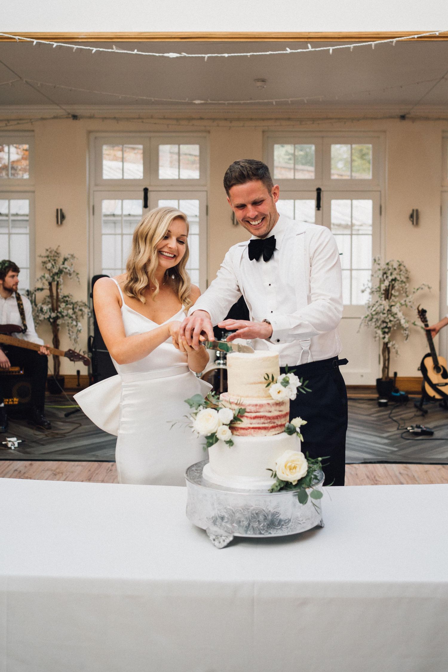 A bride and groom cut their elegant white wedding cake together during their reception celebration.