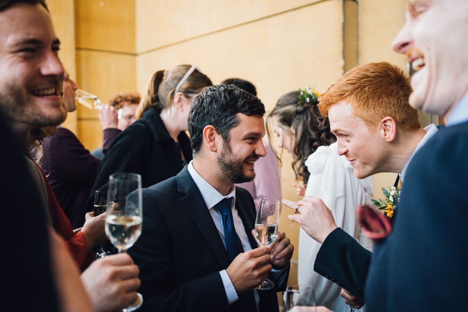Wedding guests laugh and celebrate with champagne glasses at a lively indoor wedding reception party.
