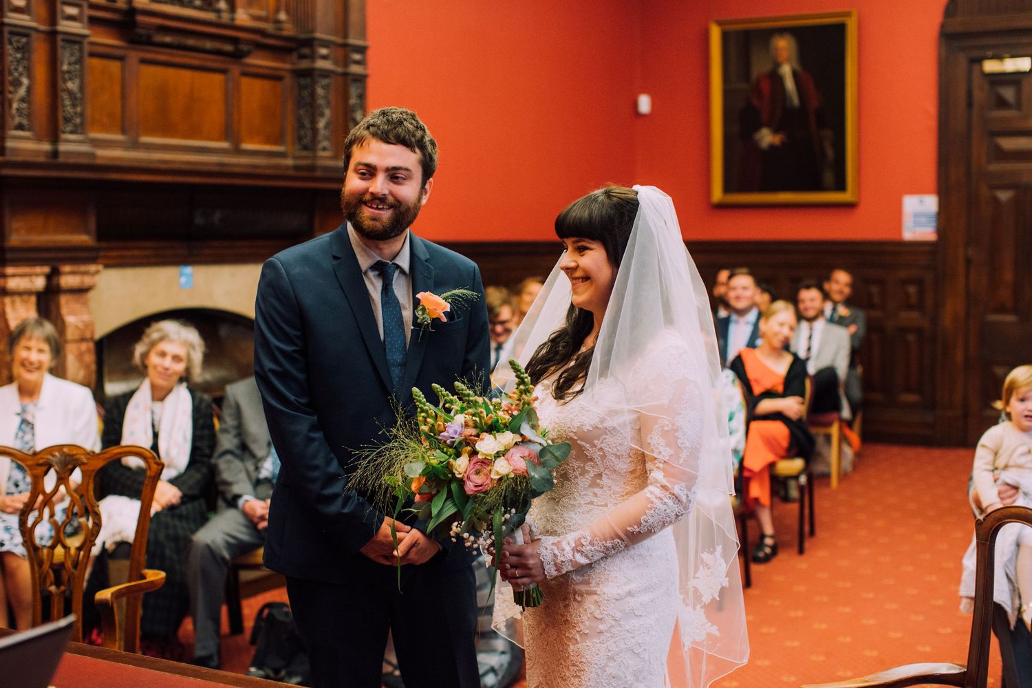 Smiling bride holding bouquet and groom standing at wedding ceremony altar in elegant wood-paneled venue.