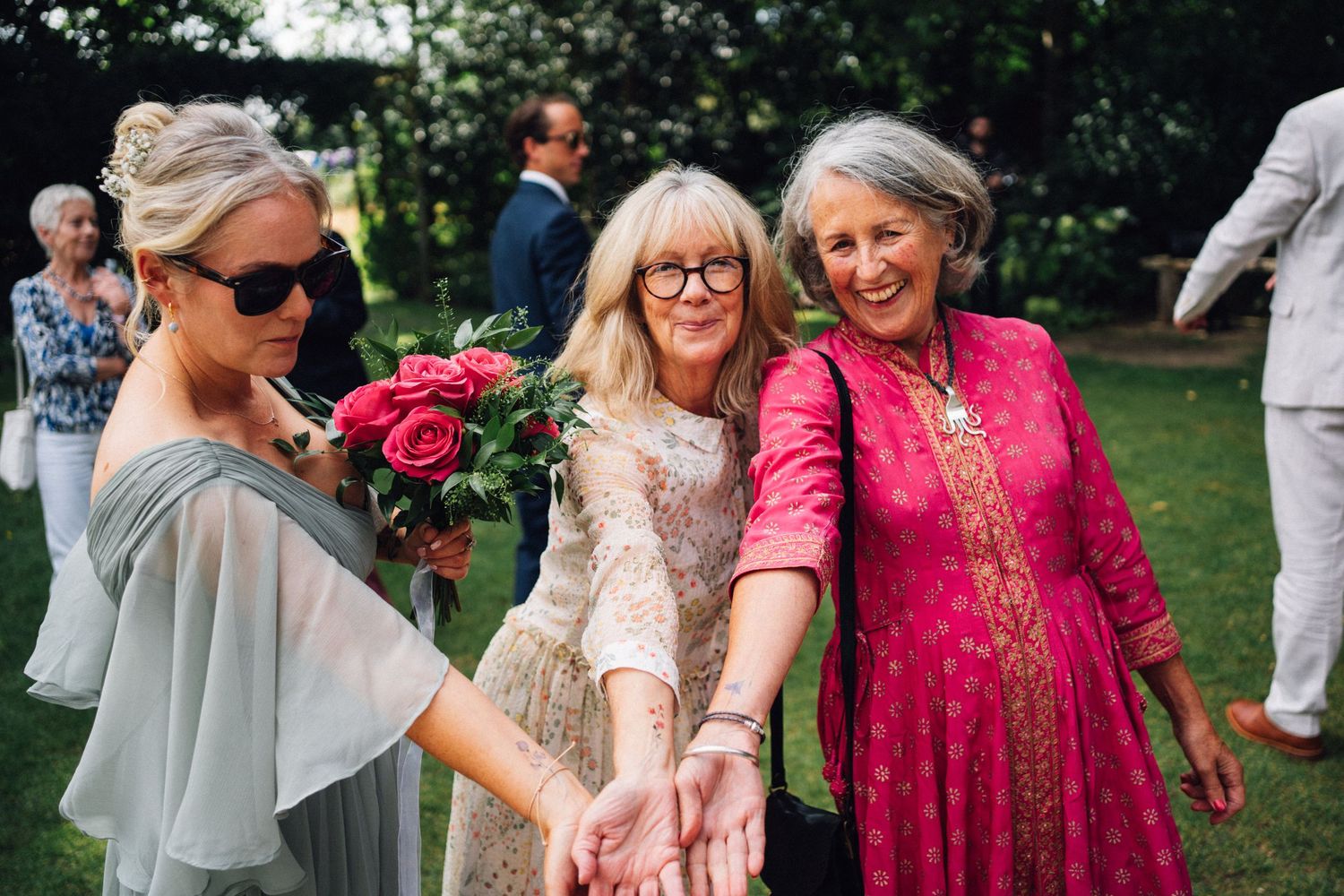 Wedding guests in colorful summer attire dancing and celebrating together on a sunny outdoor lawn.