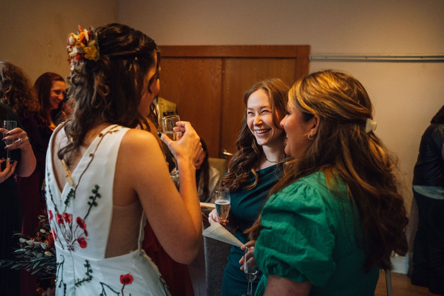 Wedding guests mingling and celebrating at an indoor reception with warm ambient lighting.
