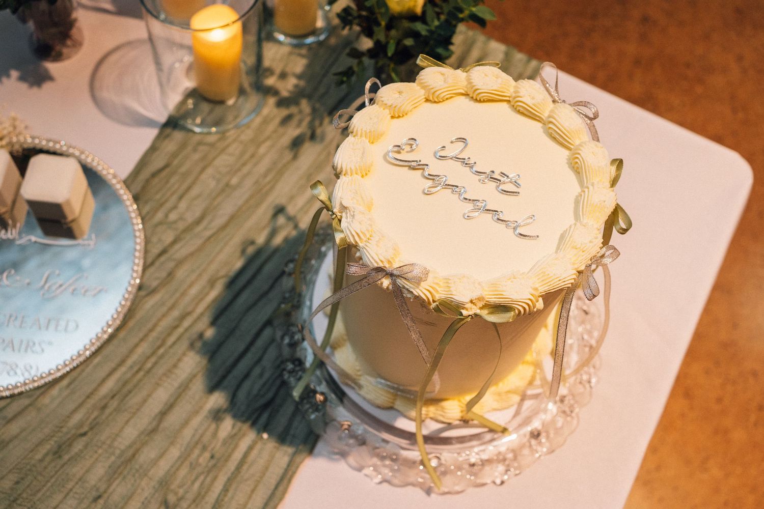 A rustic wedding table setting with glowing candles, floral arrangements, and a white cake decorated with delicate details.
