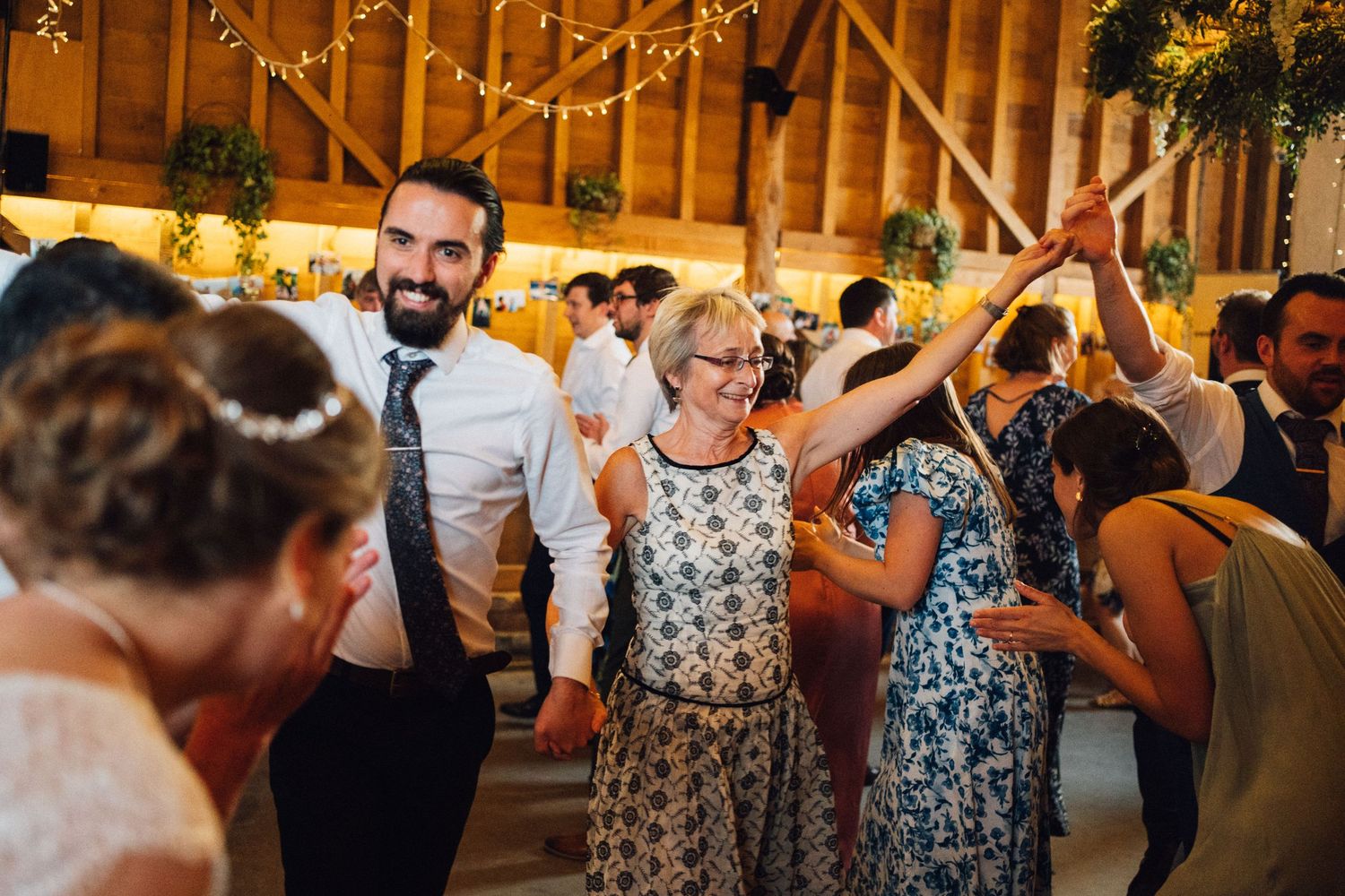 Wedding guests dancing together in a rustic barn venue decorated with string lights.