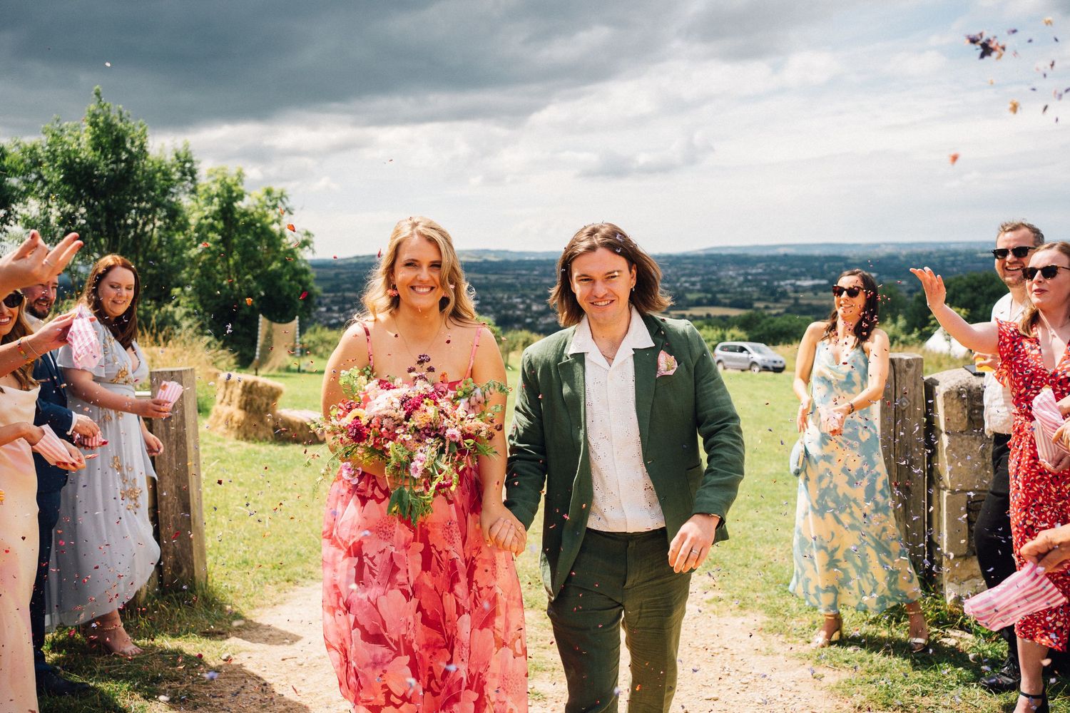 Wedding guests celebrate outdoors under cloudy skies at a countryside venue.