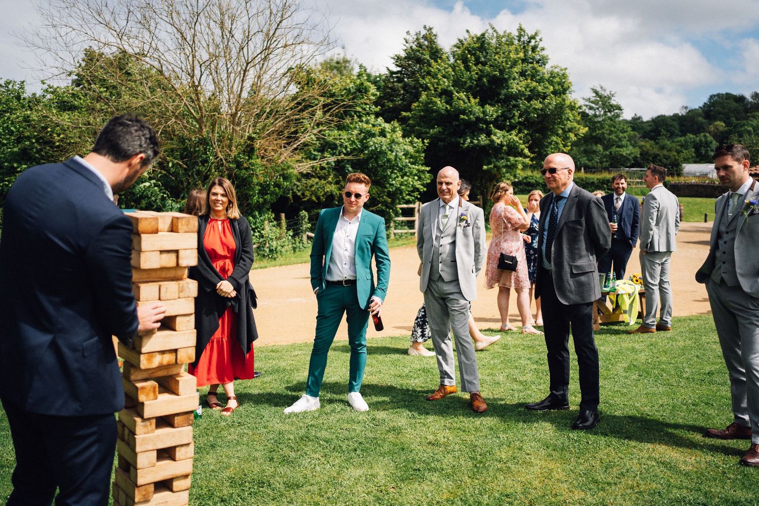 Wedding guests gathered around giant Jenga game on lawn during outdoor reception.