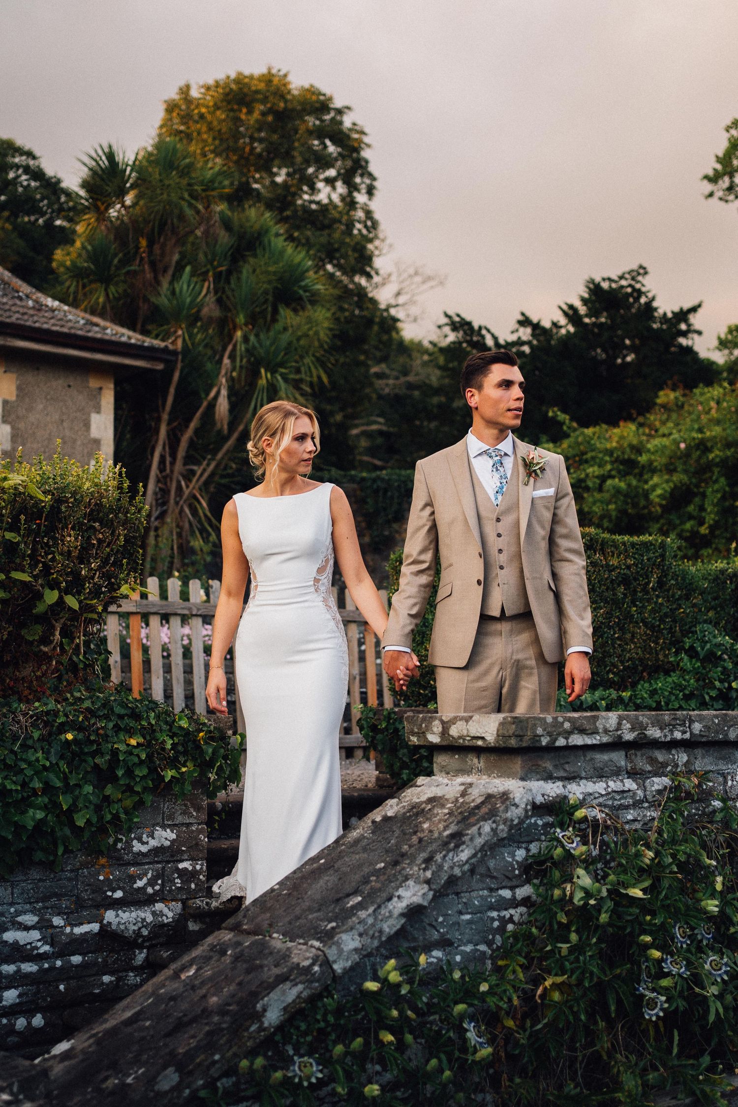 Newlyweds posing for photos on stone steps surrounded by lush garden landscaping.