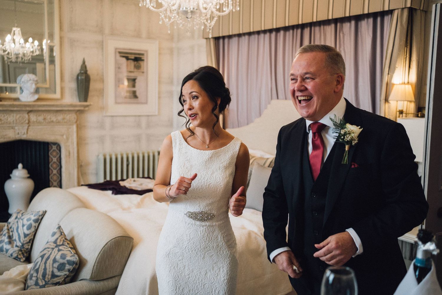 Wedding party members sharing joyful moments in an elegant room with chandelier and classic decor.