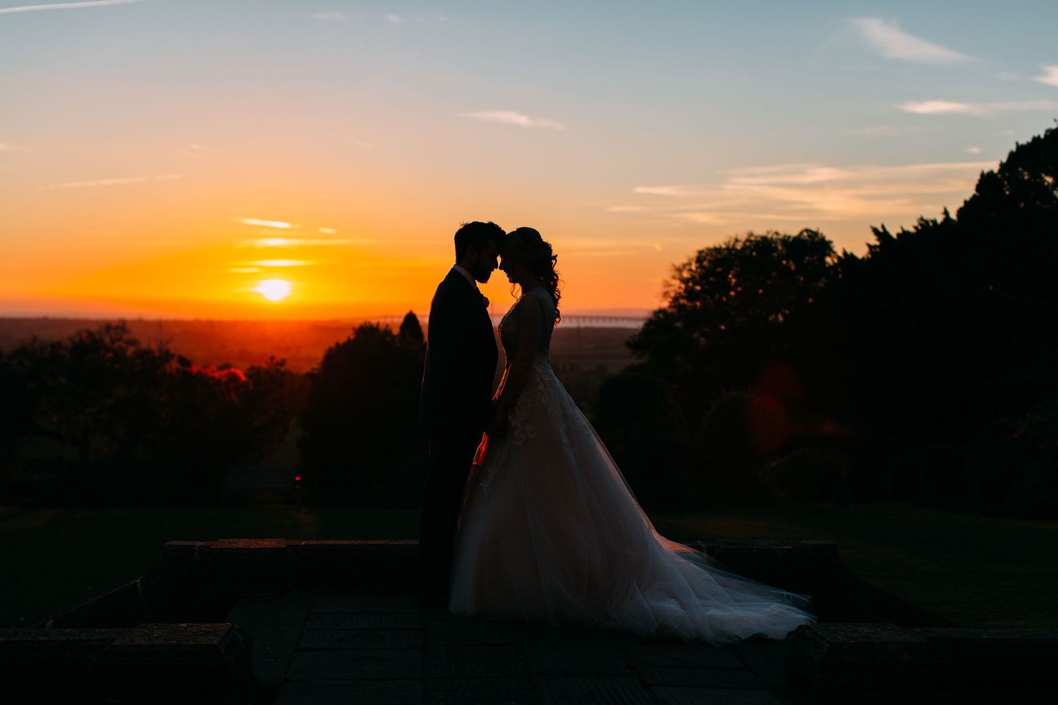 Silhouettes against dramatic orange sunset sky with trees in background.