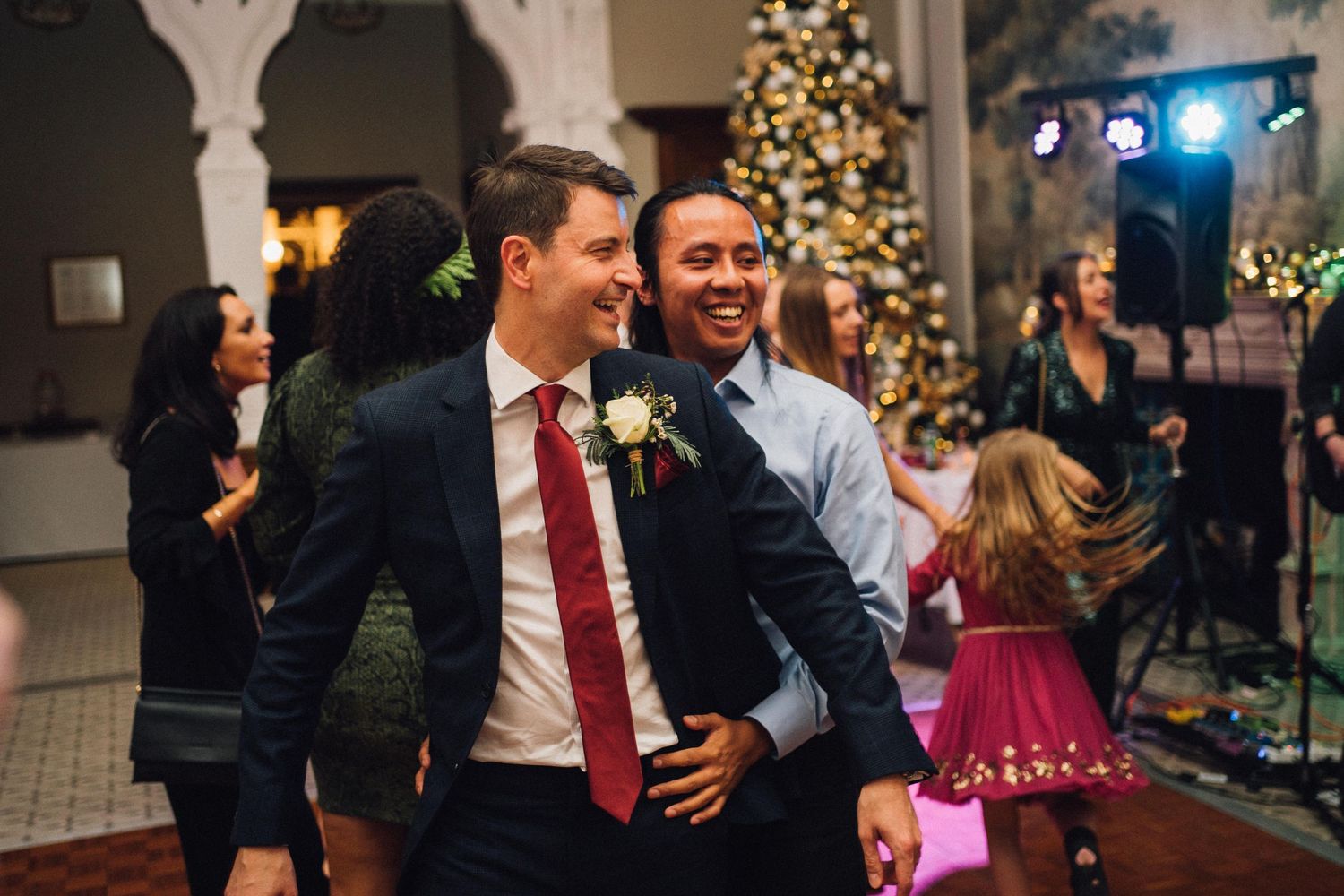 Wedding celebration with guests dancing and mingling near decorated Christmas trees and columns.