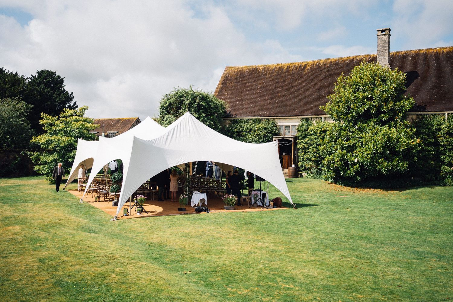 White wedding tent setup on a green lawn with rustic buildings in the background.