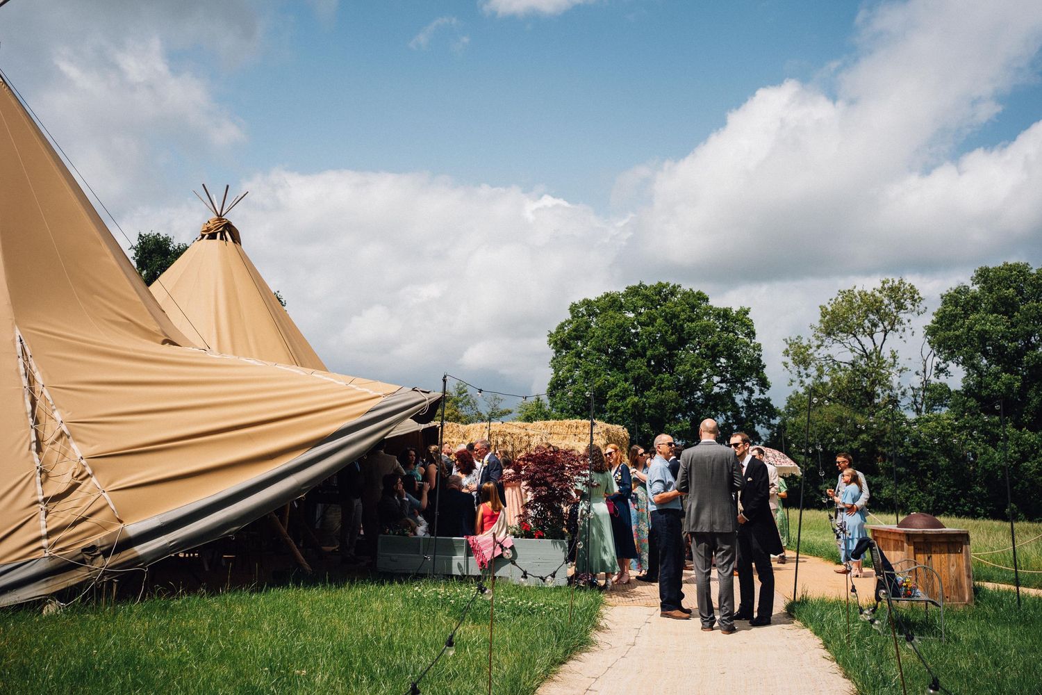 Outdoor wedding venue with tan tipi tents set against a backdrop of blue sky and white clouds.