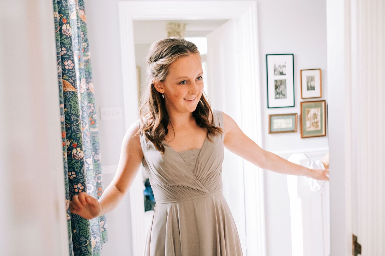 Person in beige dress moving gracefully against white walls and floral curtains.