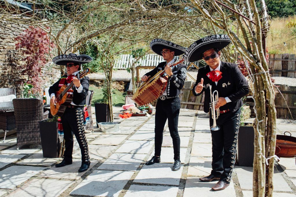 Three mariachi musicians in traditional black outfits performing on a stone patio.