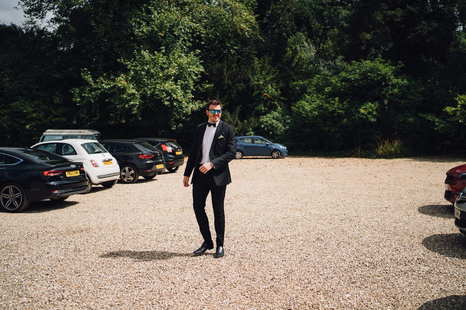 Stone courtyard with parked cars and people in formal attire walking through the space.