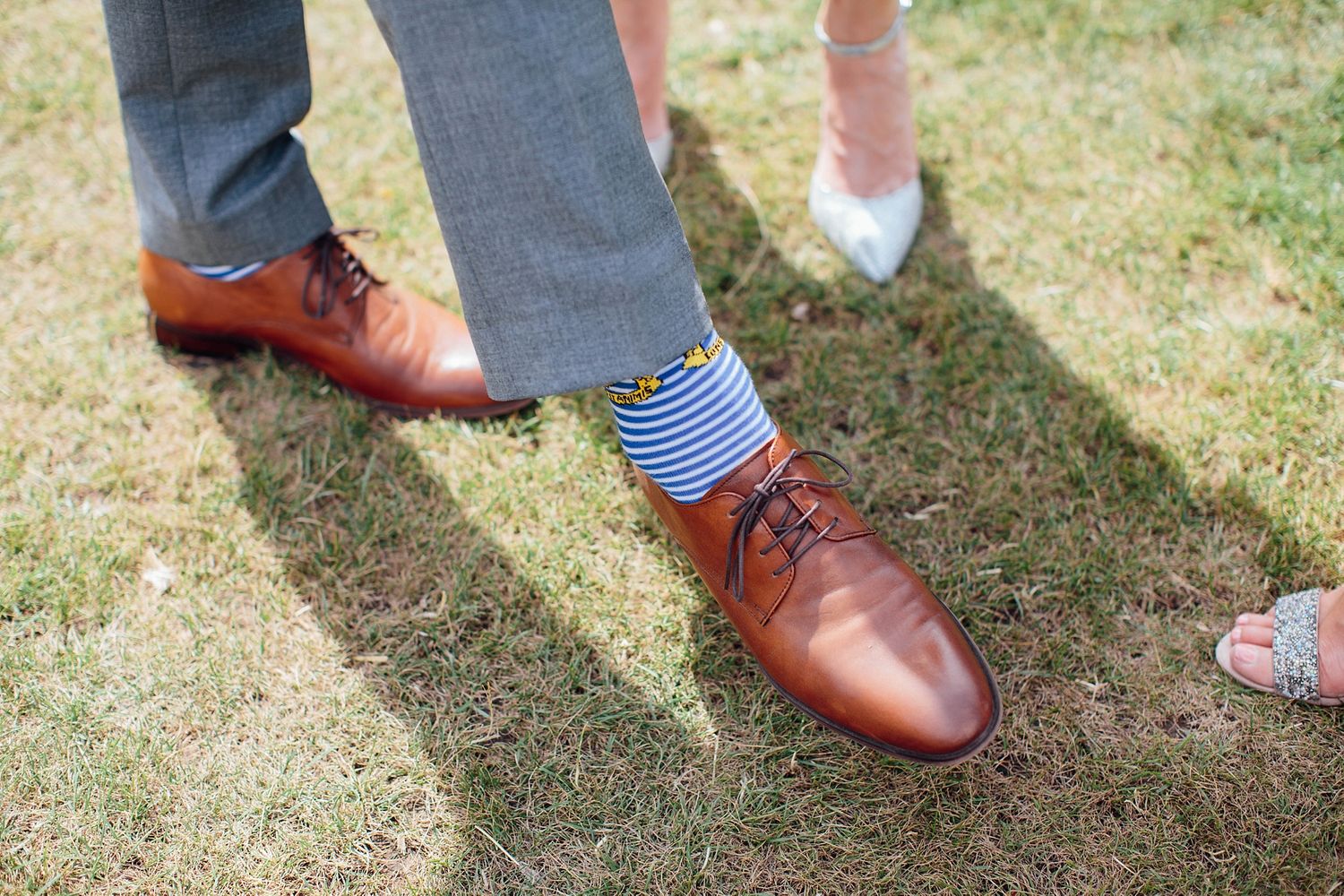 Brown leather dress shoes with striped socks on grass at outdoor event.