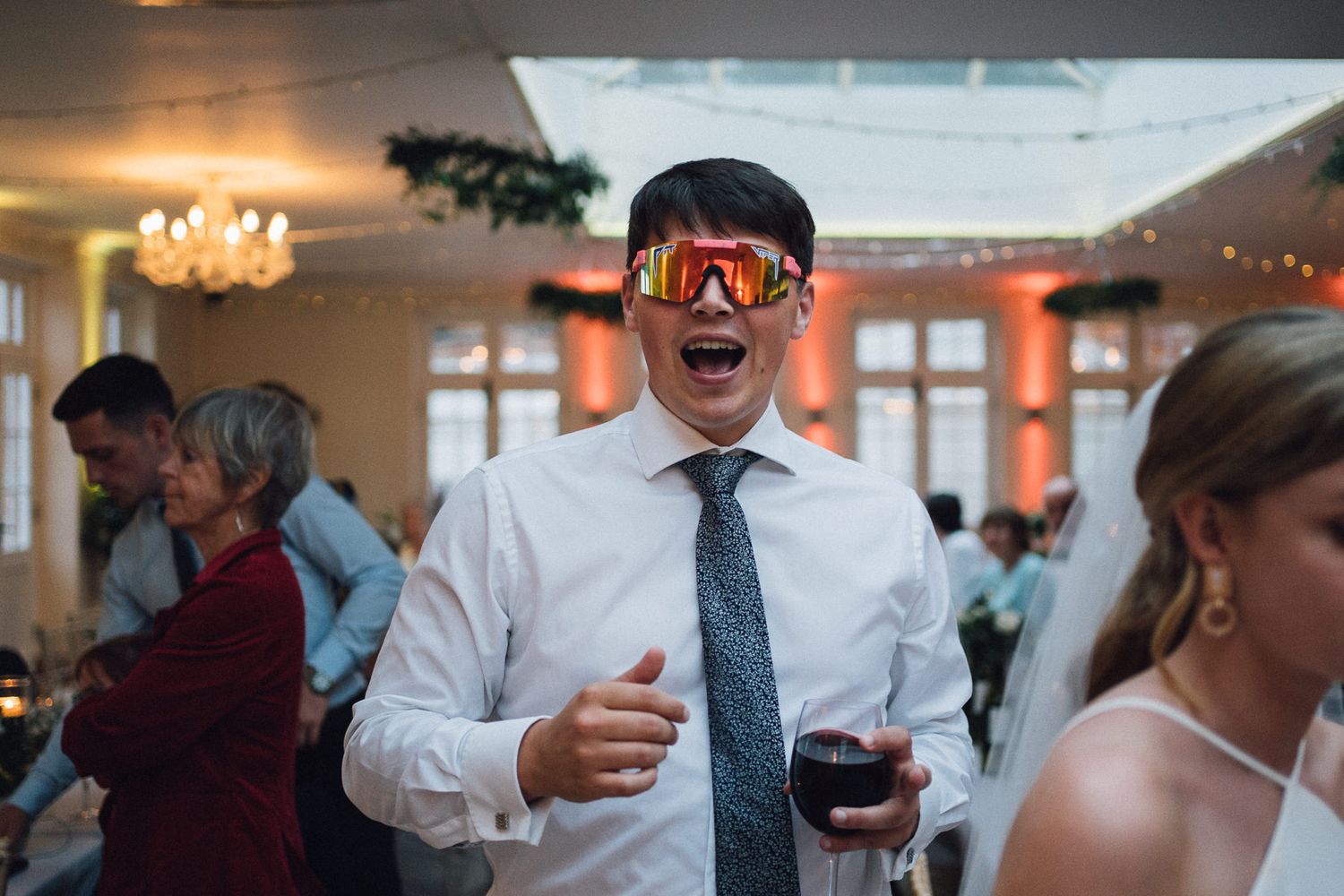 A guest enjoying the wedding reception while wearing reflective sunglasses indoors.