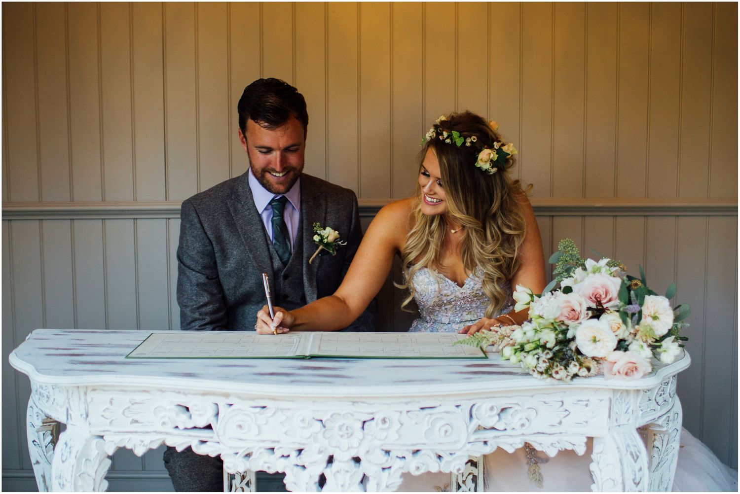 Wedding couple signs documents at an ornate white table during their ceremony.