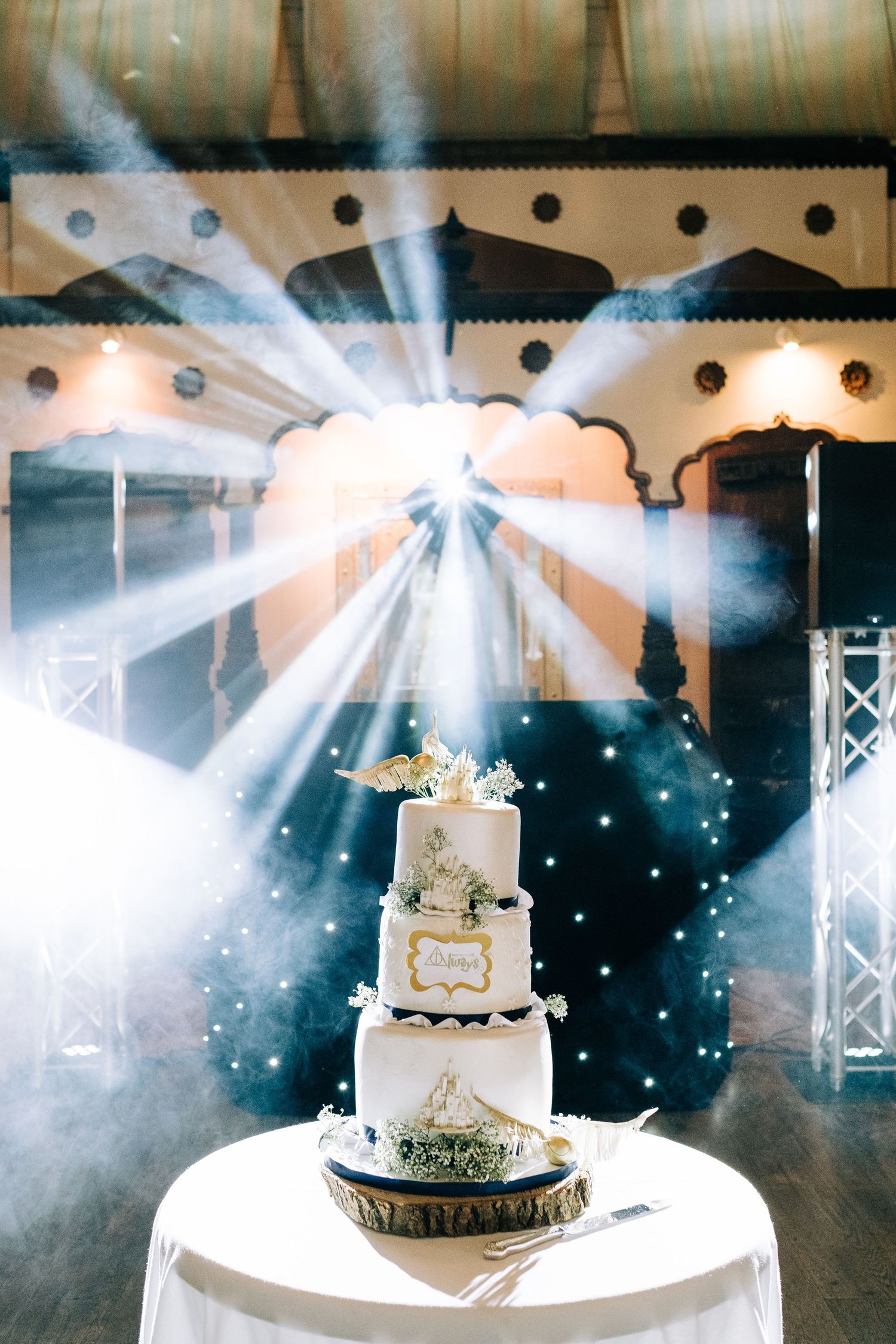 Elegant wedding cake illuminated by dramatic spotlights and smoke effects at an indoor reception venue.