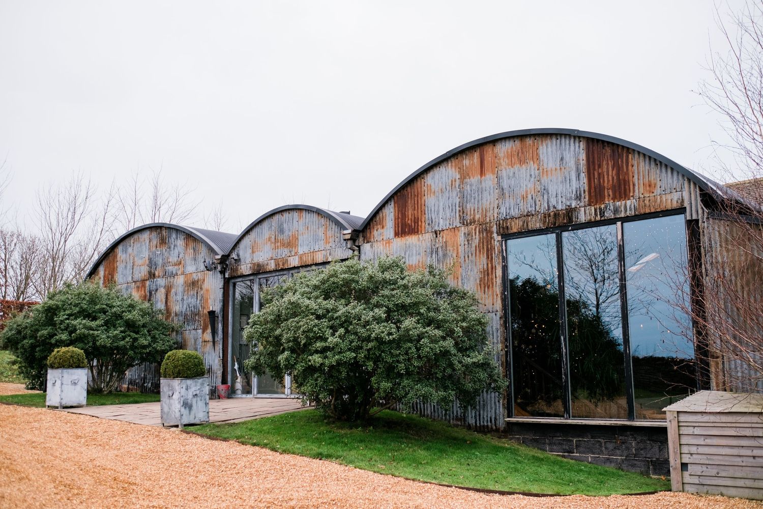 Panoramic view of rustic barn wedding venue exterior with curved metal roof and surrounding landscape.