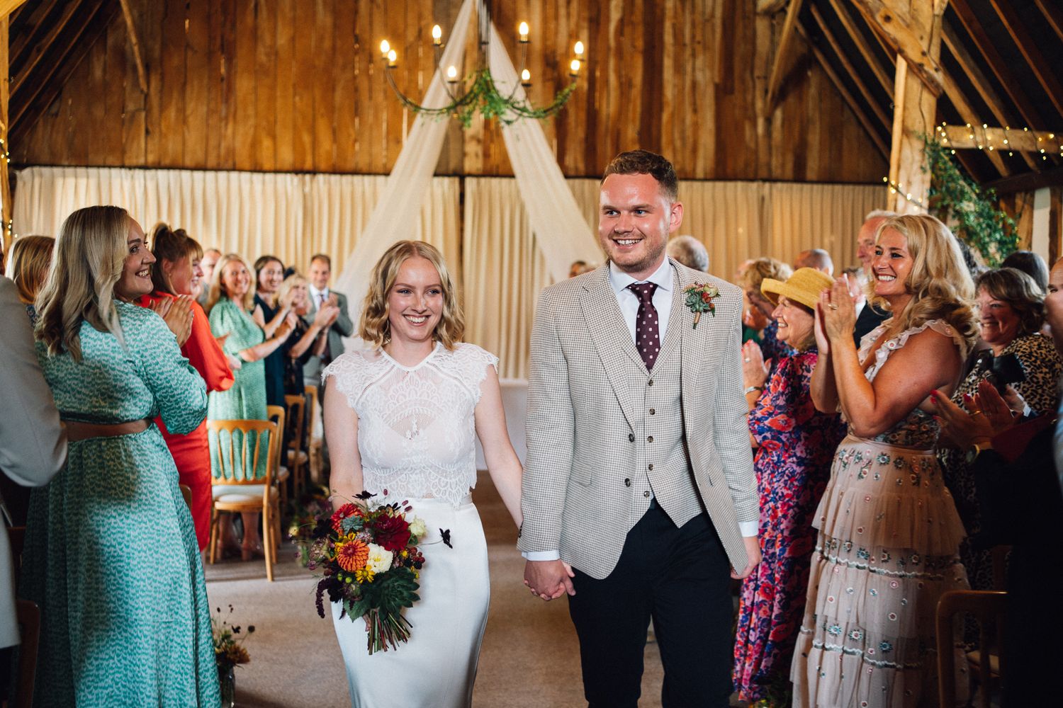 Wedding party celebrates inside a rustic wooden barn venue with string lights and decorative elements.