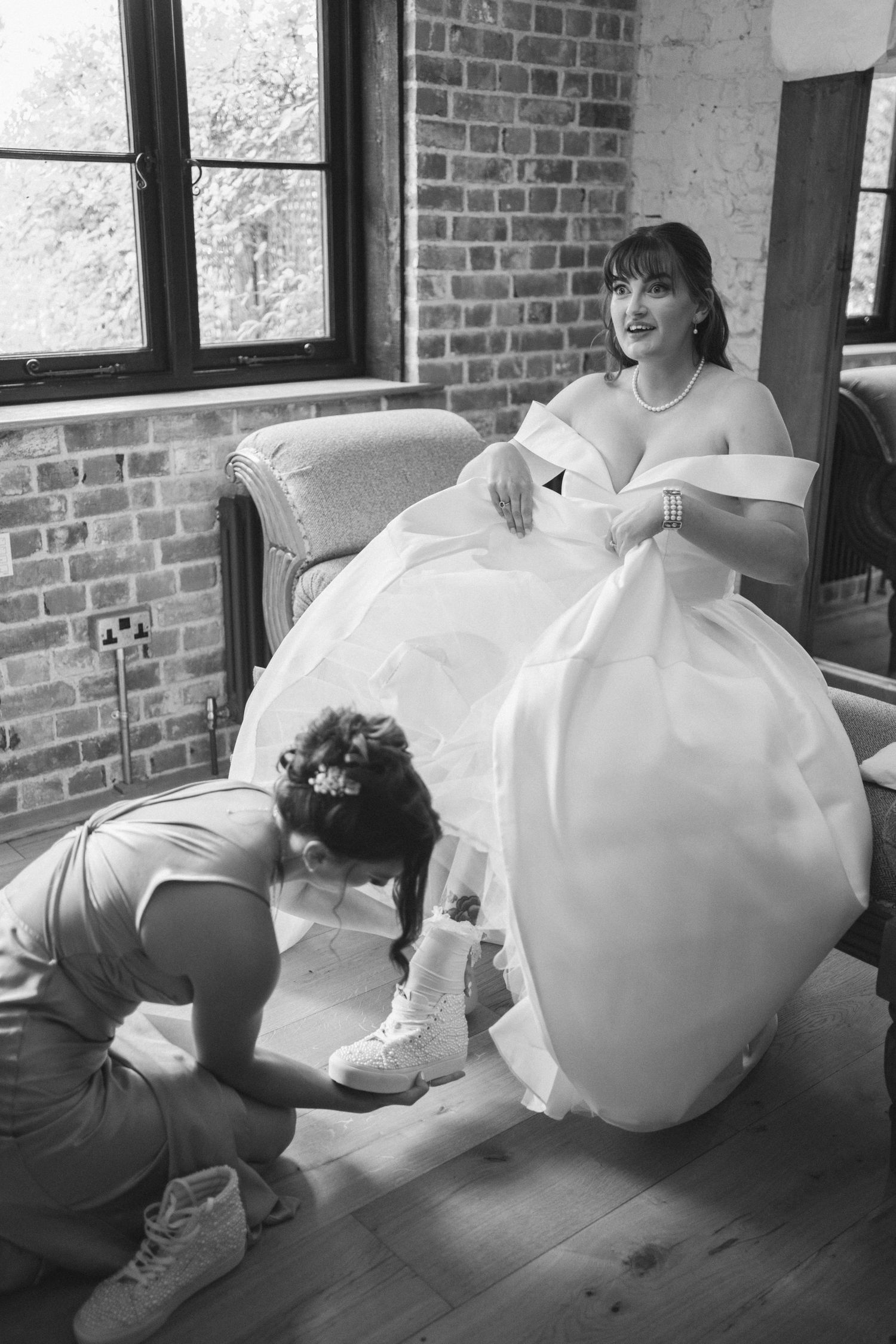 Black and white sequence shows a bride in a white dress being helped to sit on a chair against a brick wall.