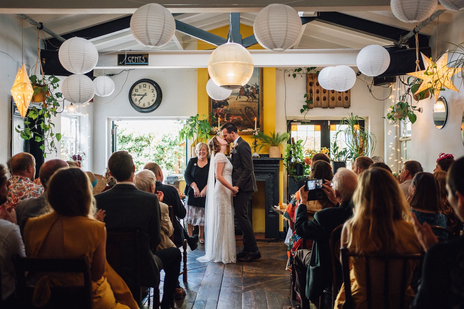 White paper lanterns and string lights decorate a lively indoor celebration space filled with mingling guests.