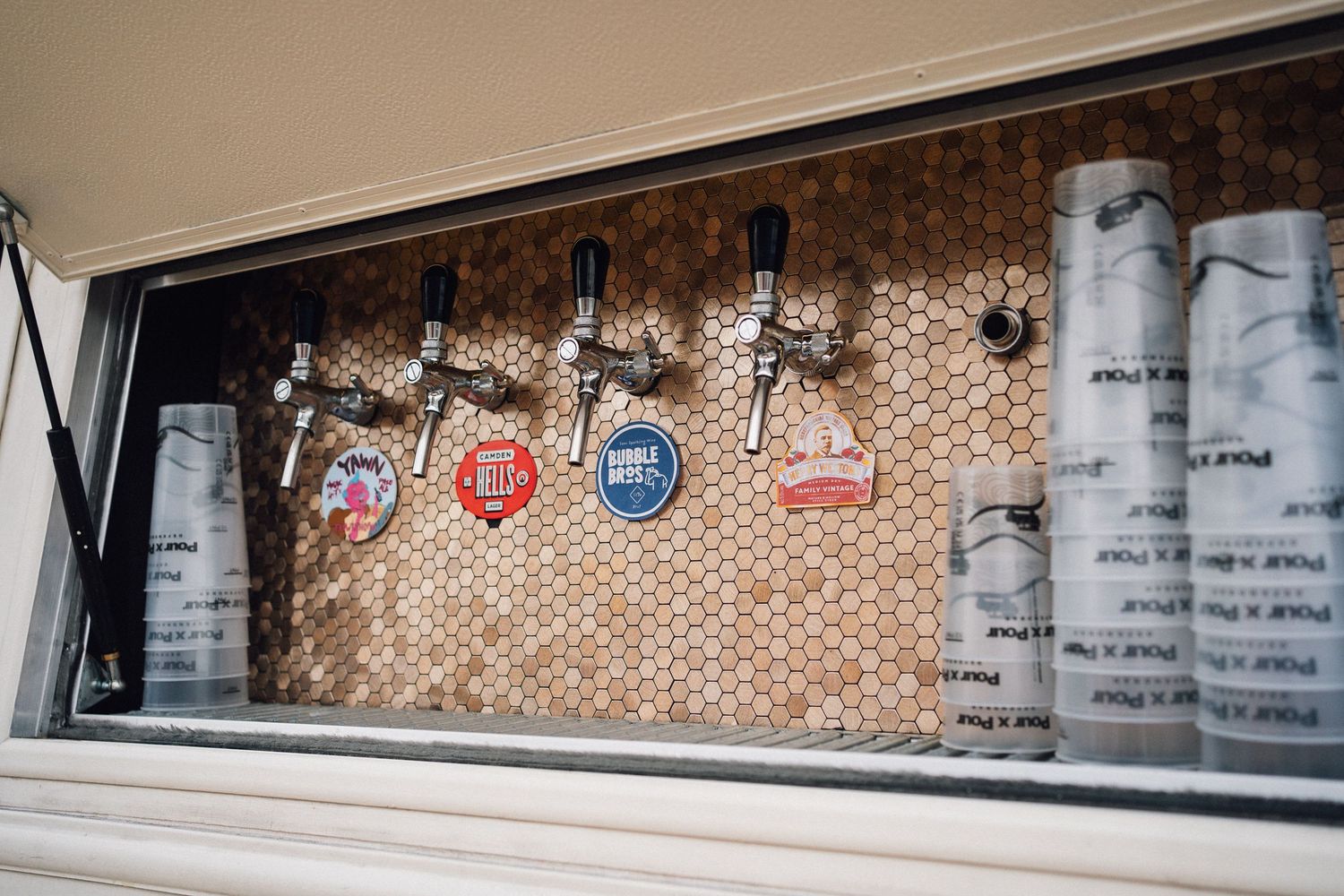 Beer taps mounted on a rustic brick wall with kegs visible through a window display.