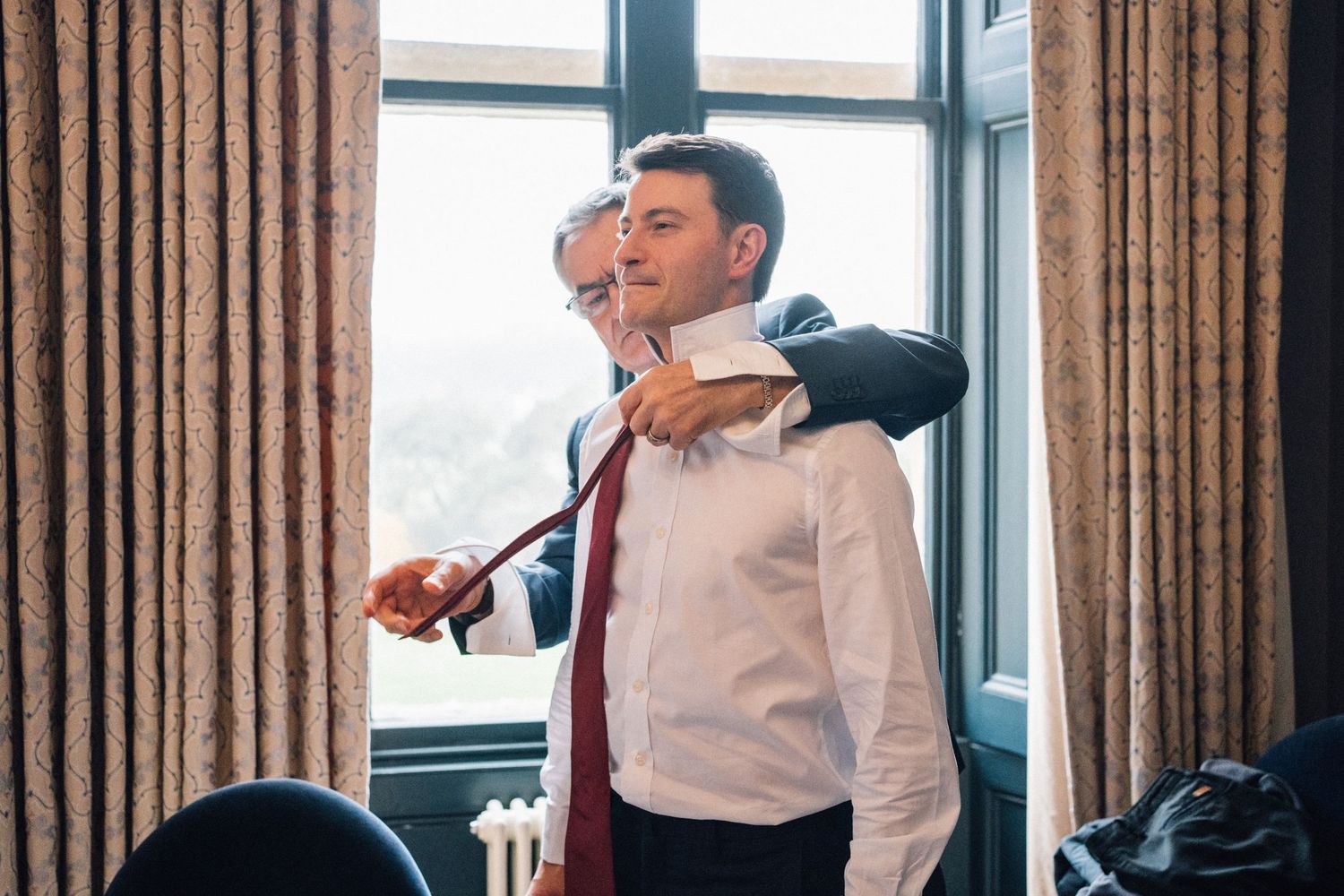 Candid moments of wedding preparation in a bright room with floor-length curtains.