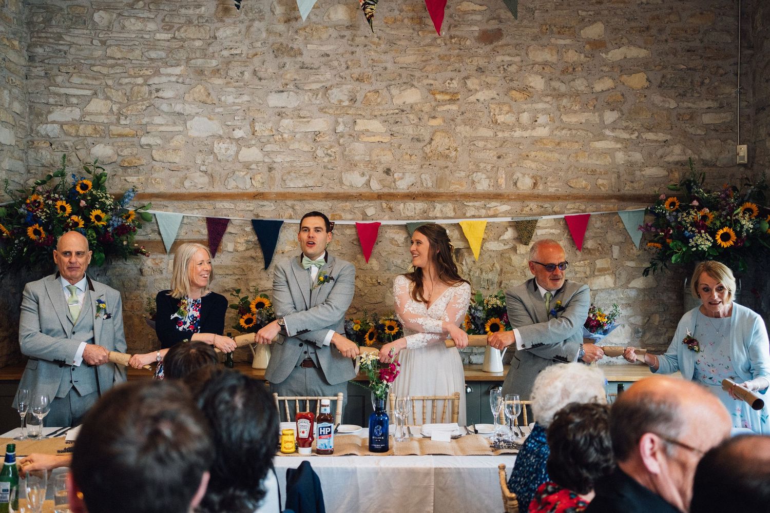 Long dining tables set up for wedding reception with stone wall backdrop and hanging bunting flags.