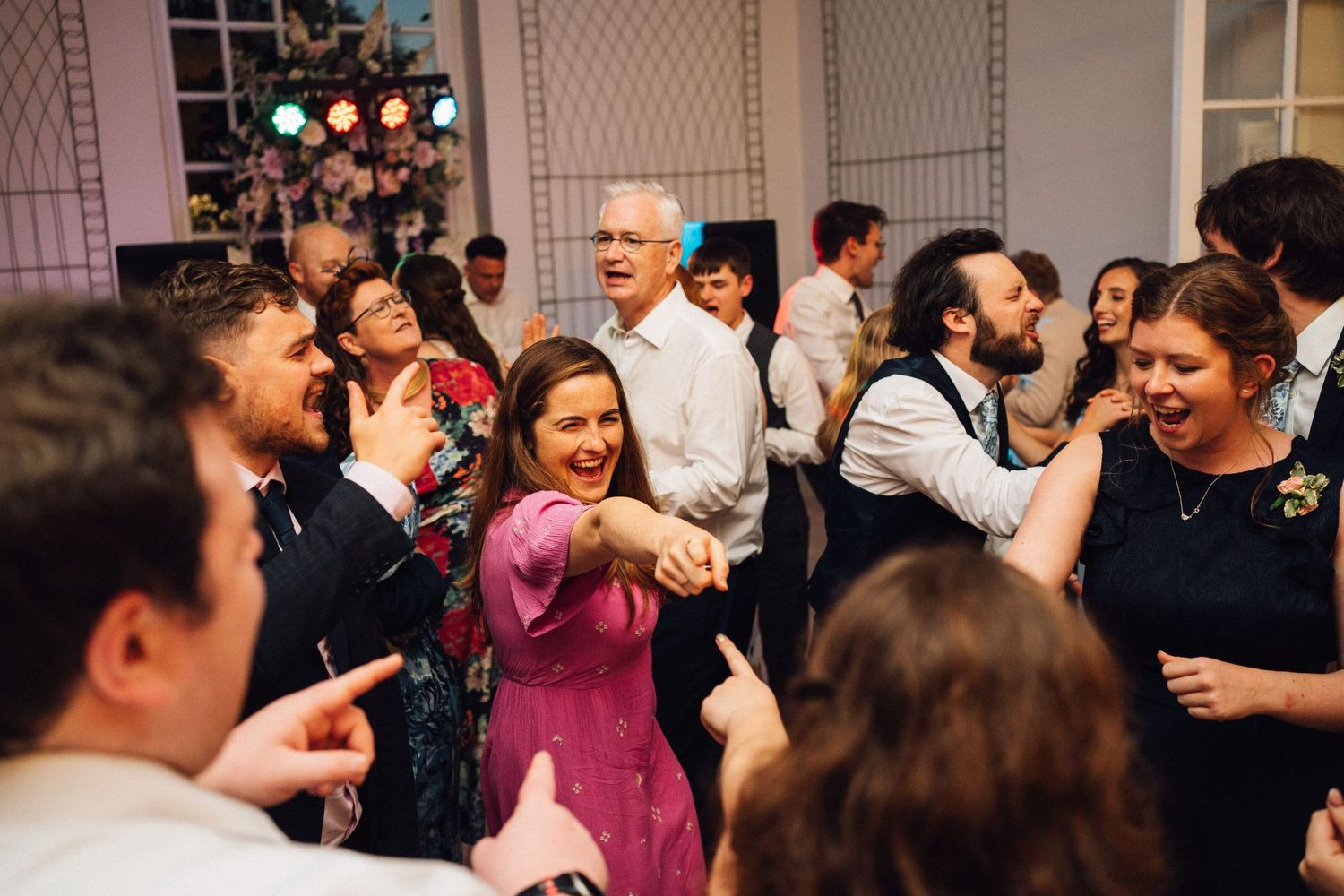 Joyful wedding guests dancing and laughing during reception party celebrations.