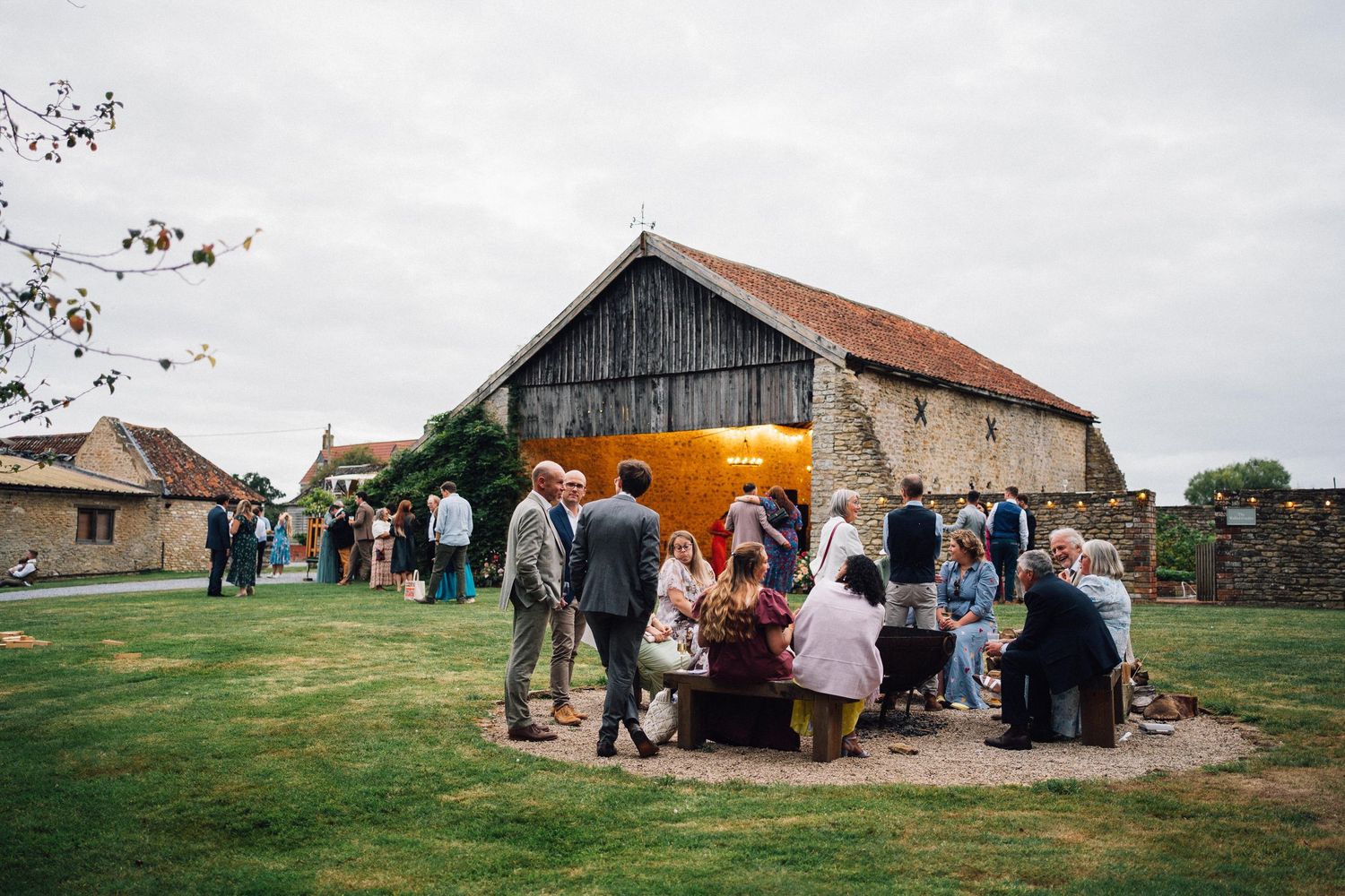 Wedding guests gather outside rustic barn venue during daytime celebration.